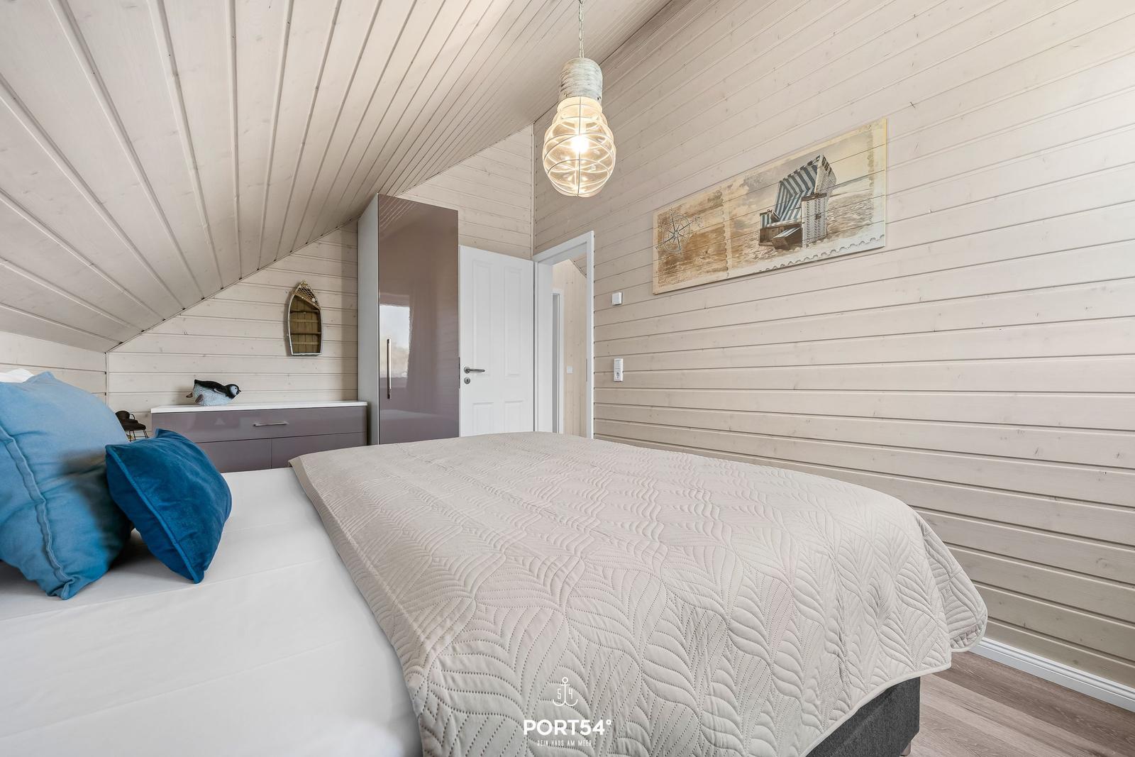 Schlafzimmer mit Bett, Kleiderschrank und Wandbild. Holzwand und Decke.