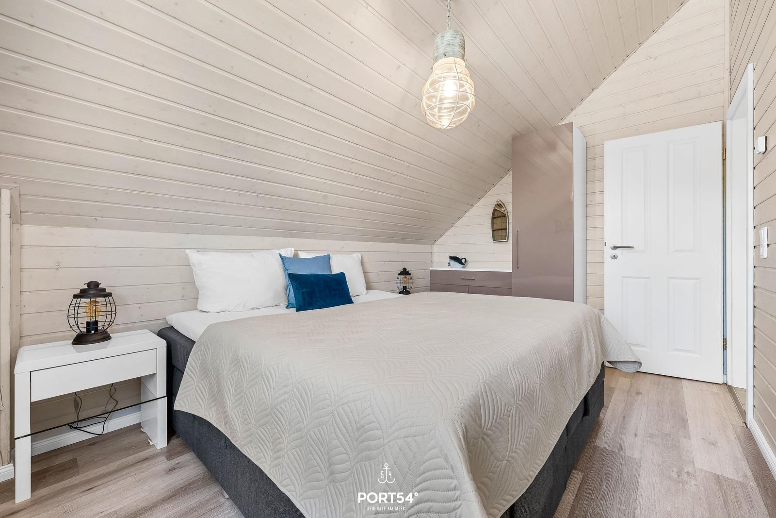 Schlafzimmer mit Dachschrägen, Bett, Nachttisch und Schrank.