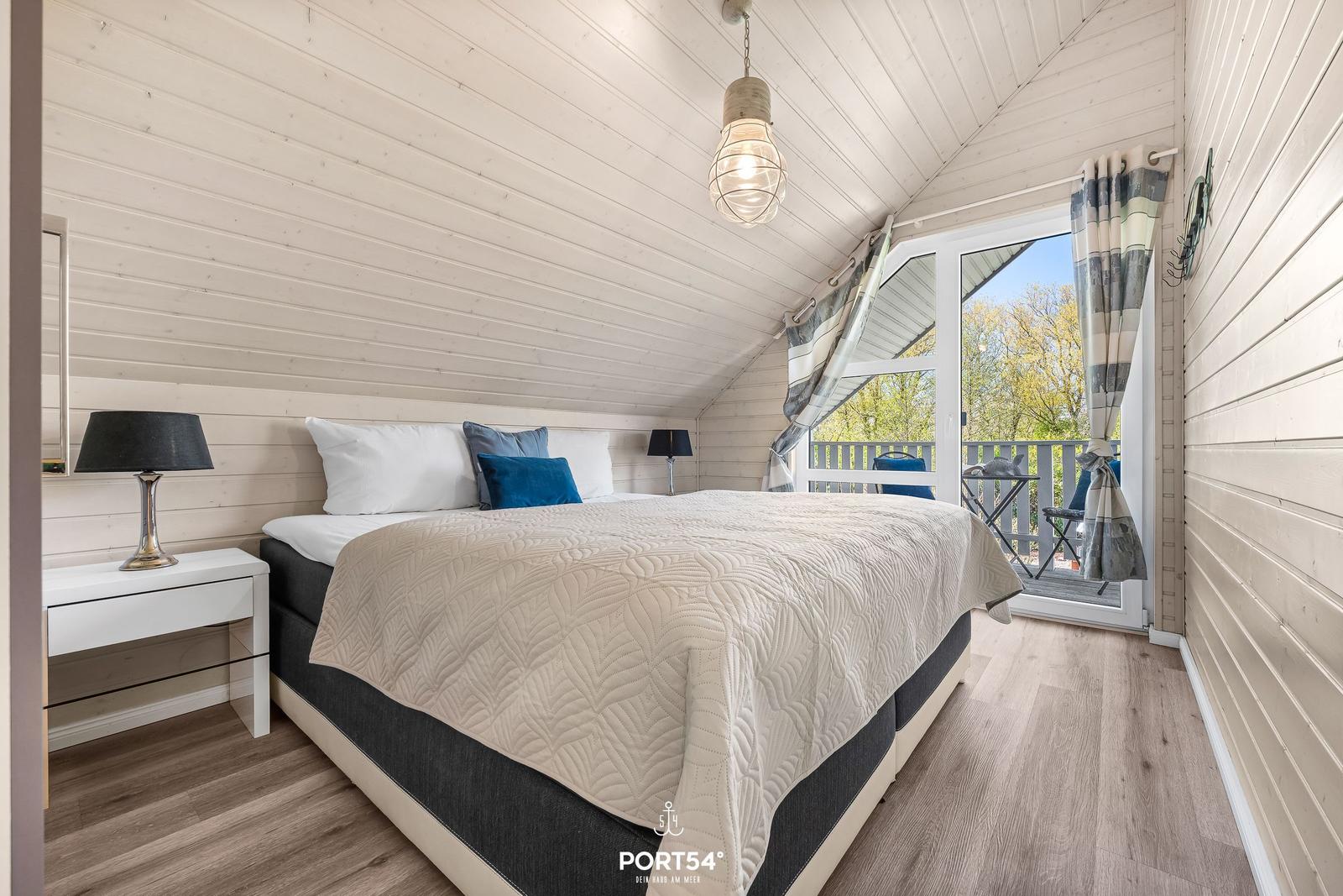 Schlafzimmer mit Doppelbett, Balkon und Holzwandverkleidung.