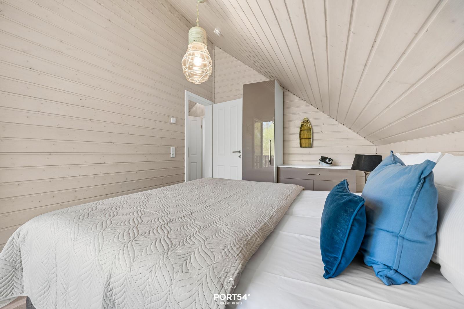 Schlafzimmer mit Bett, blauen Kissen und Holzwand
