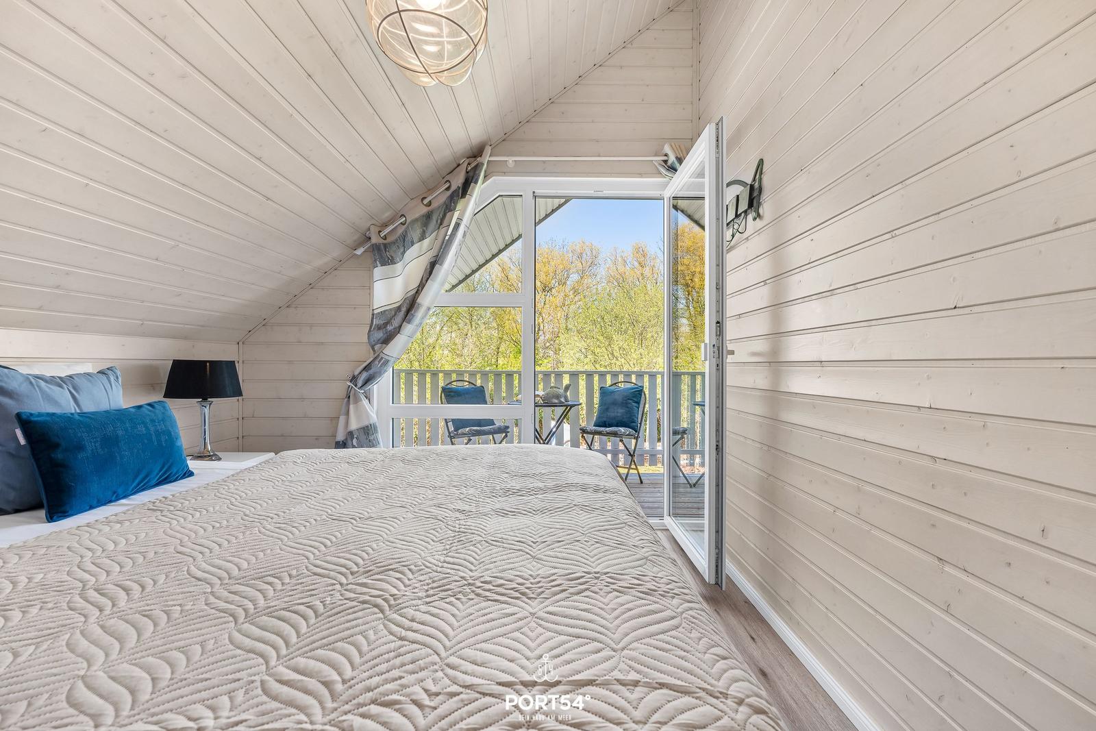 Schlafzimmer mit Balkon und Holzwandverkleidung. Bett mit Decke und Kissen.