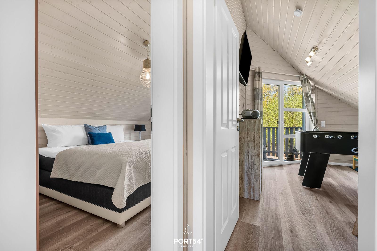 Schlafzimmer mit Bett und Blick auf Spielzimmer mit Tischfußball.