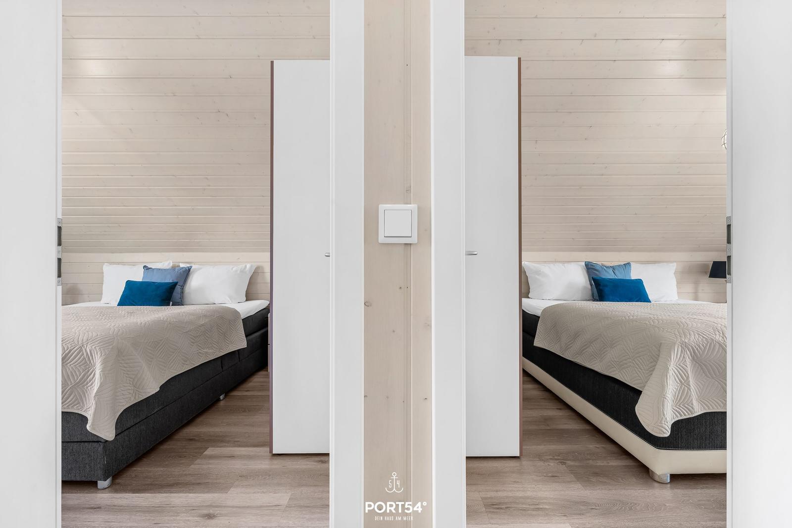 Zwei Schlafzimmer mit Betten und Holzwänden sind durch eine Tür sichtbar.