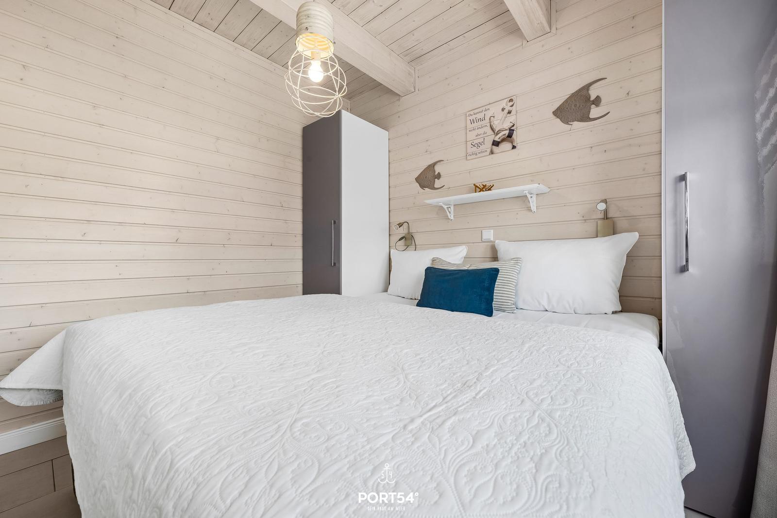 Schlafzimmer mit weißem Bett, Holzwand und Kleiderschränken.