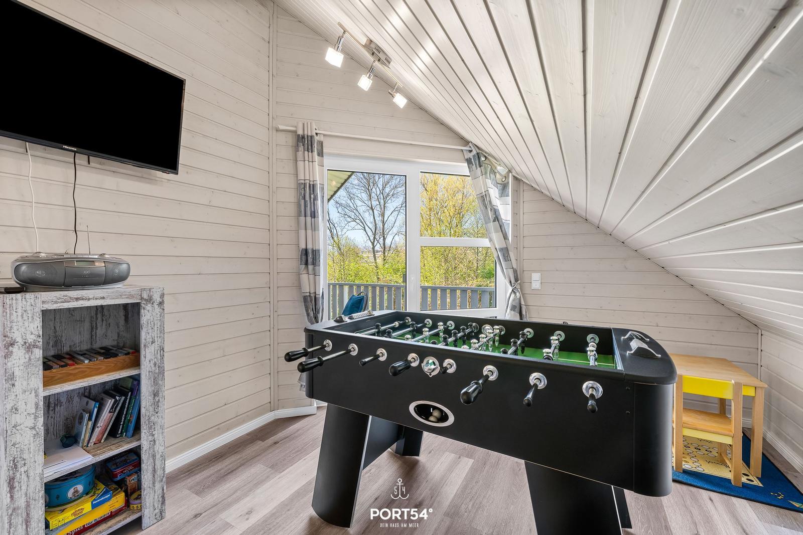 Fußballtisch in einem Raum mit Holzwand und Fenster zur Terrasse.