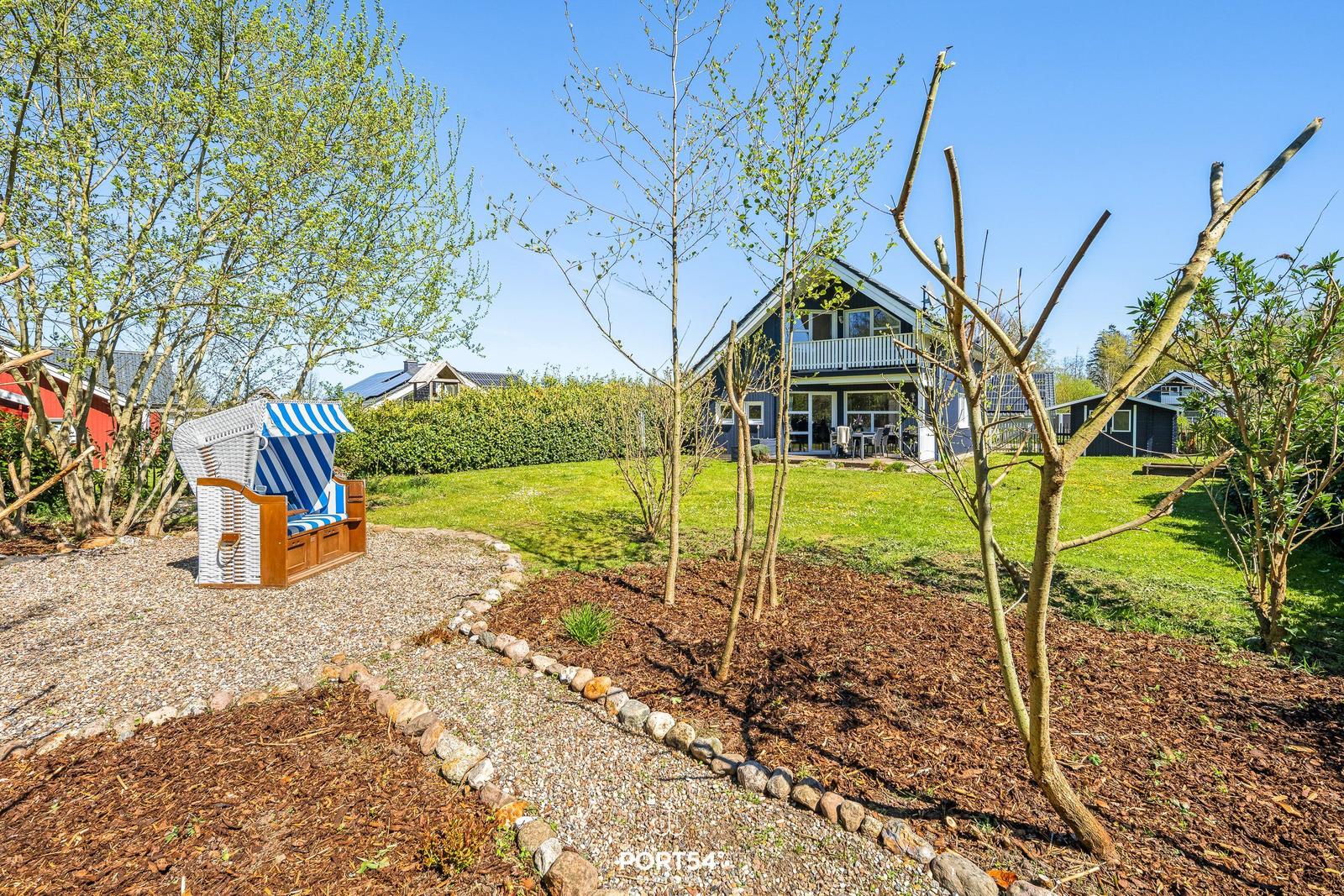 Ein blau gestrichenes Haus mit Balkon und Garten. Eine Strandliege steht auf Kies.