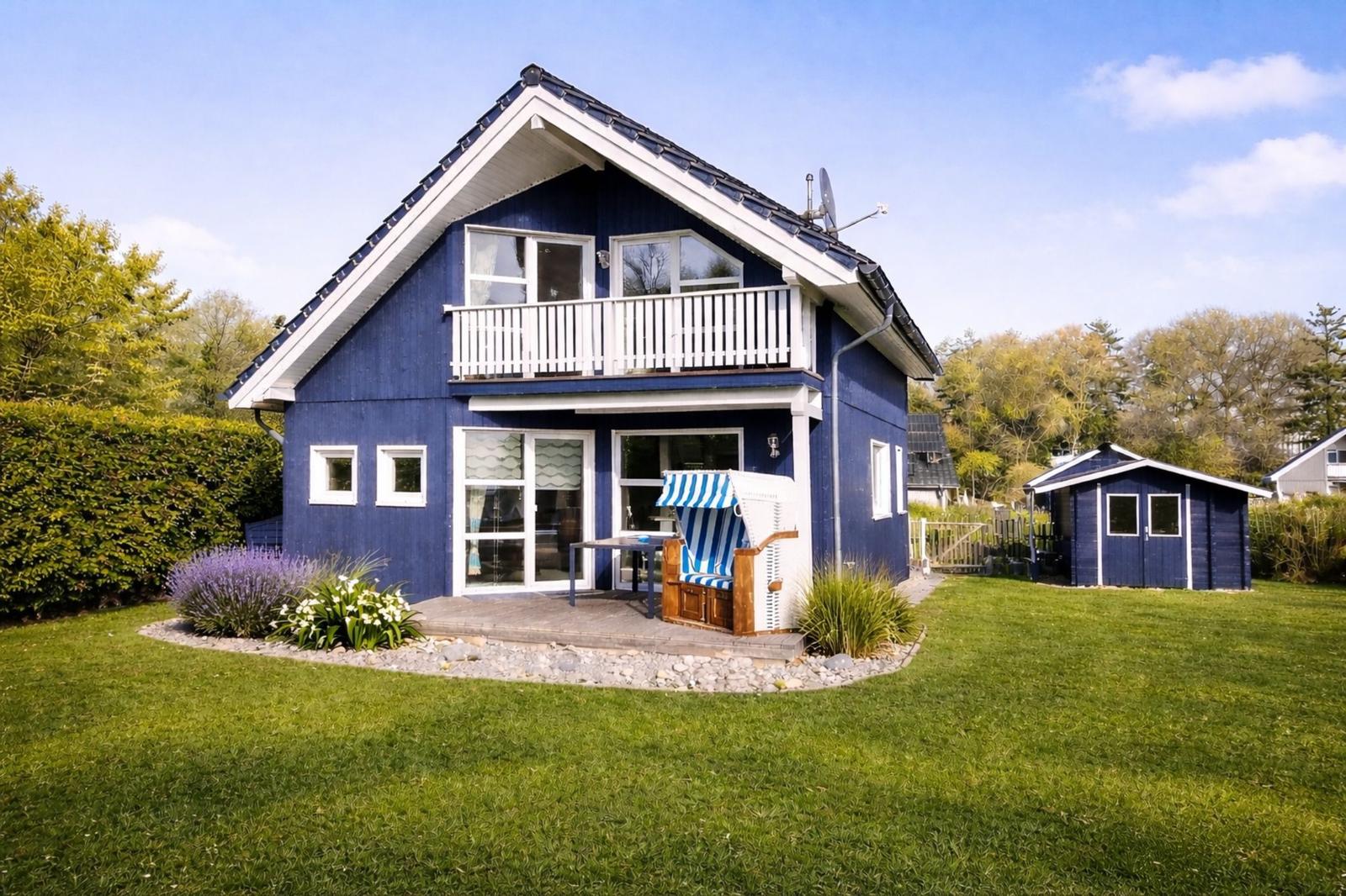 Blau gestrichenes Ferienhaus mit Balkon und Garten. Ein Strandkorb steht auf der Terrasse.