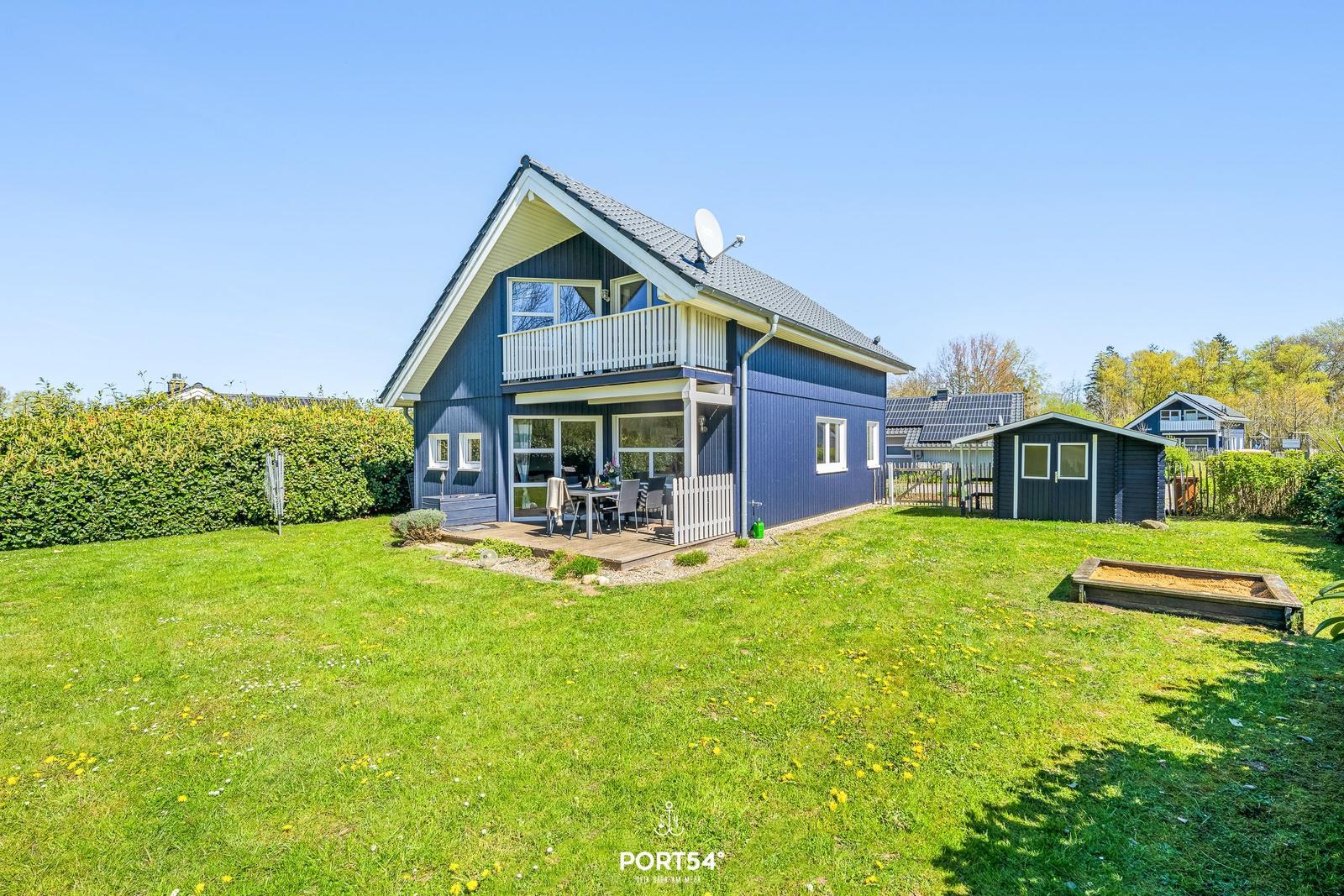 Blau gestrichenes Haus mit Terrasse und Garten. Nebenan steht ein kleiner Schuppen.