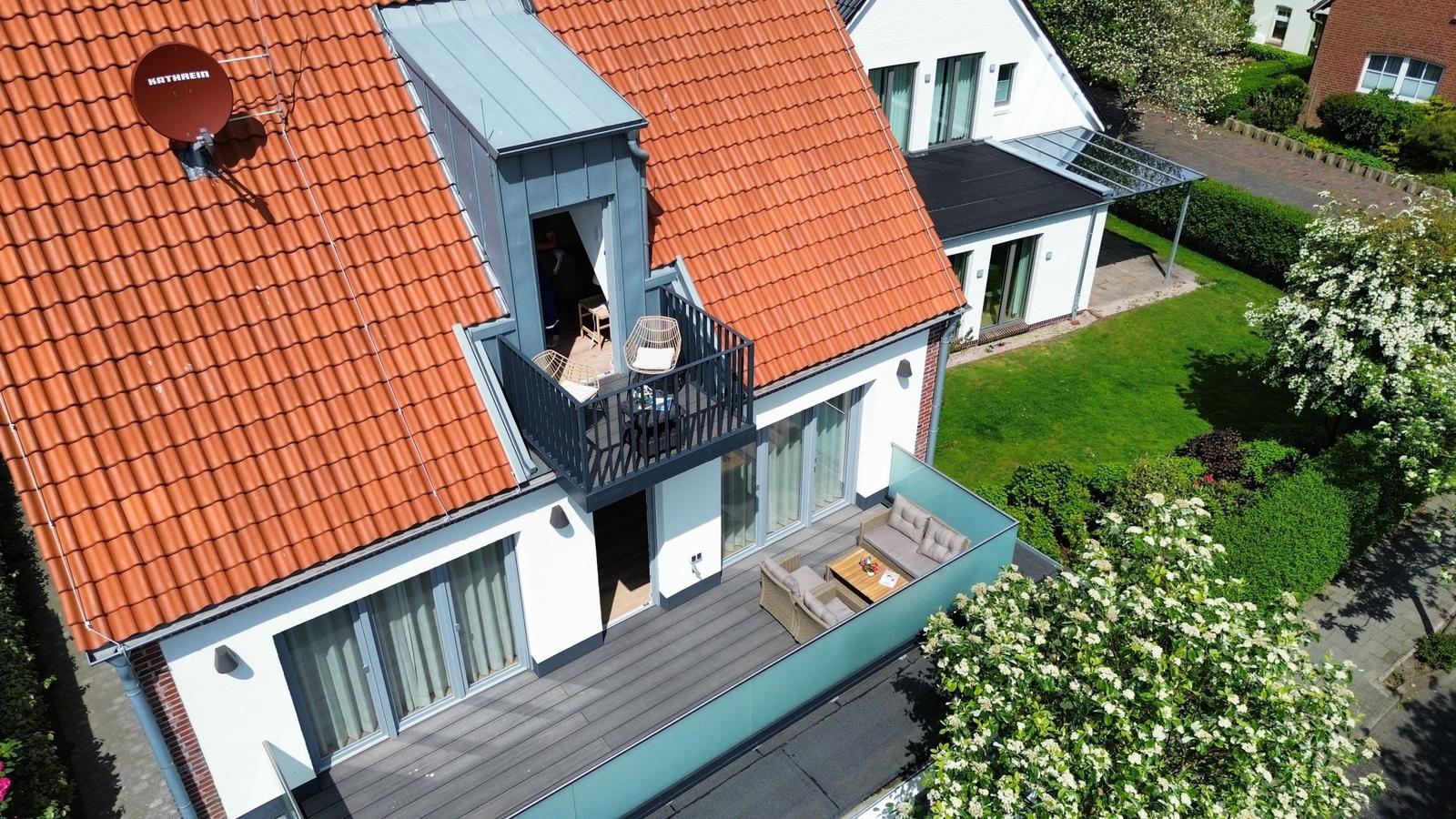 Haus mit Balkon und Terrasse, umgeben von Grünflächen und Blumen.
