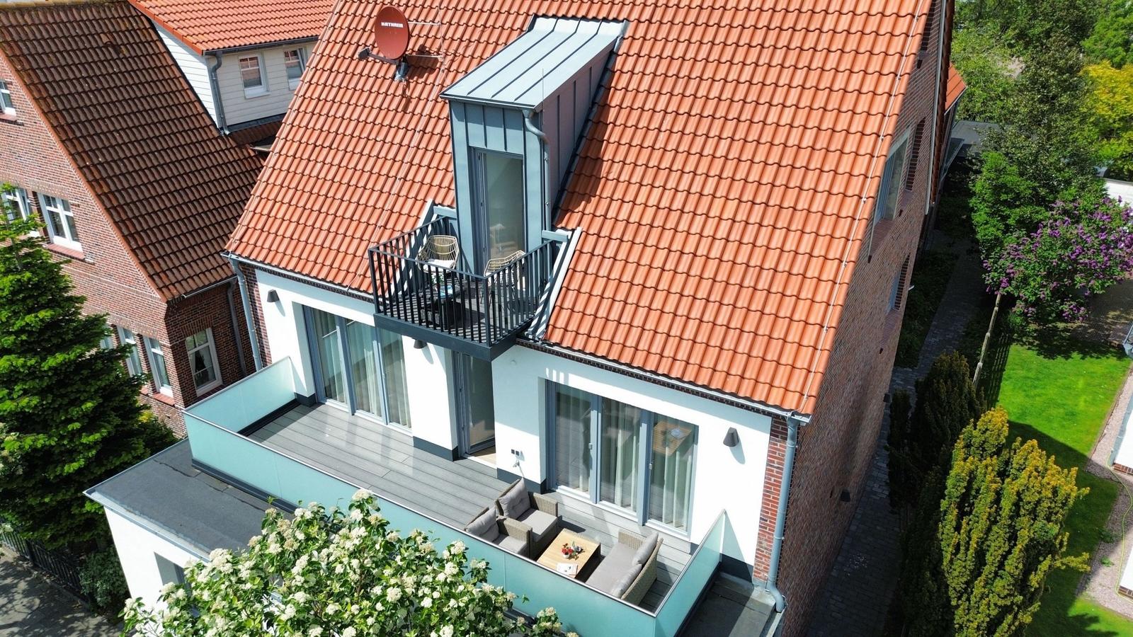Haus mit Terrasse und Balkon, umgeben von Grünflächen und Bäumen.