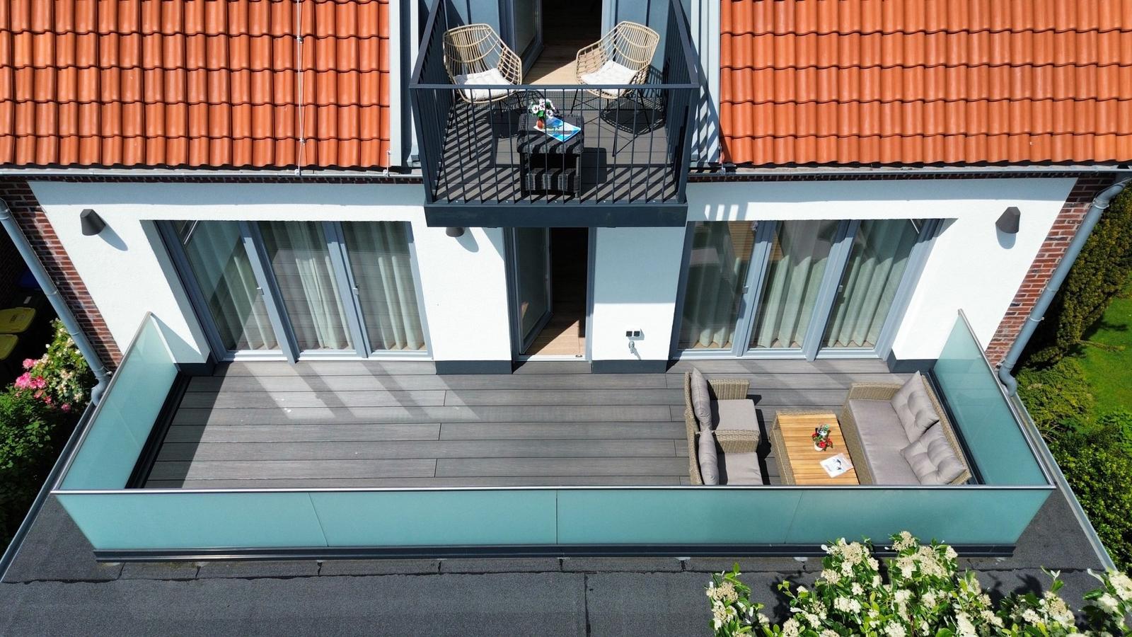 Terrasse mit Sitzgruppe und kleinem Balkon mit zwei Stühlen und Tisch.