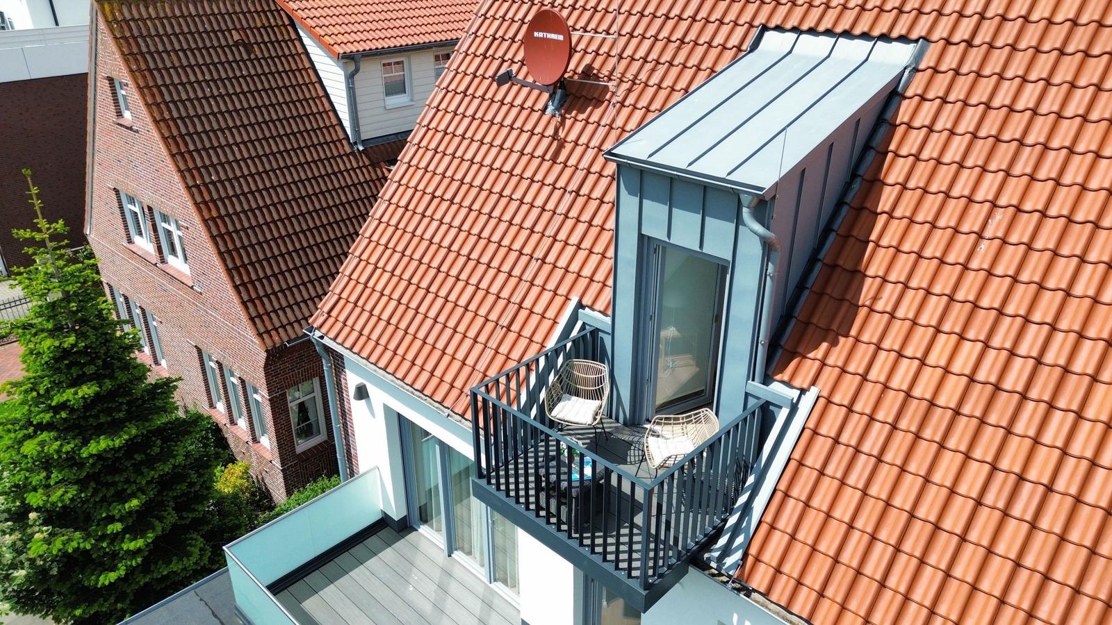 Dachterrasse mit Sitzgelegenheiten und Blick auf rote Ziegeldächer.