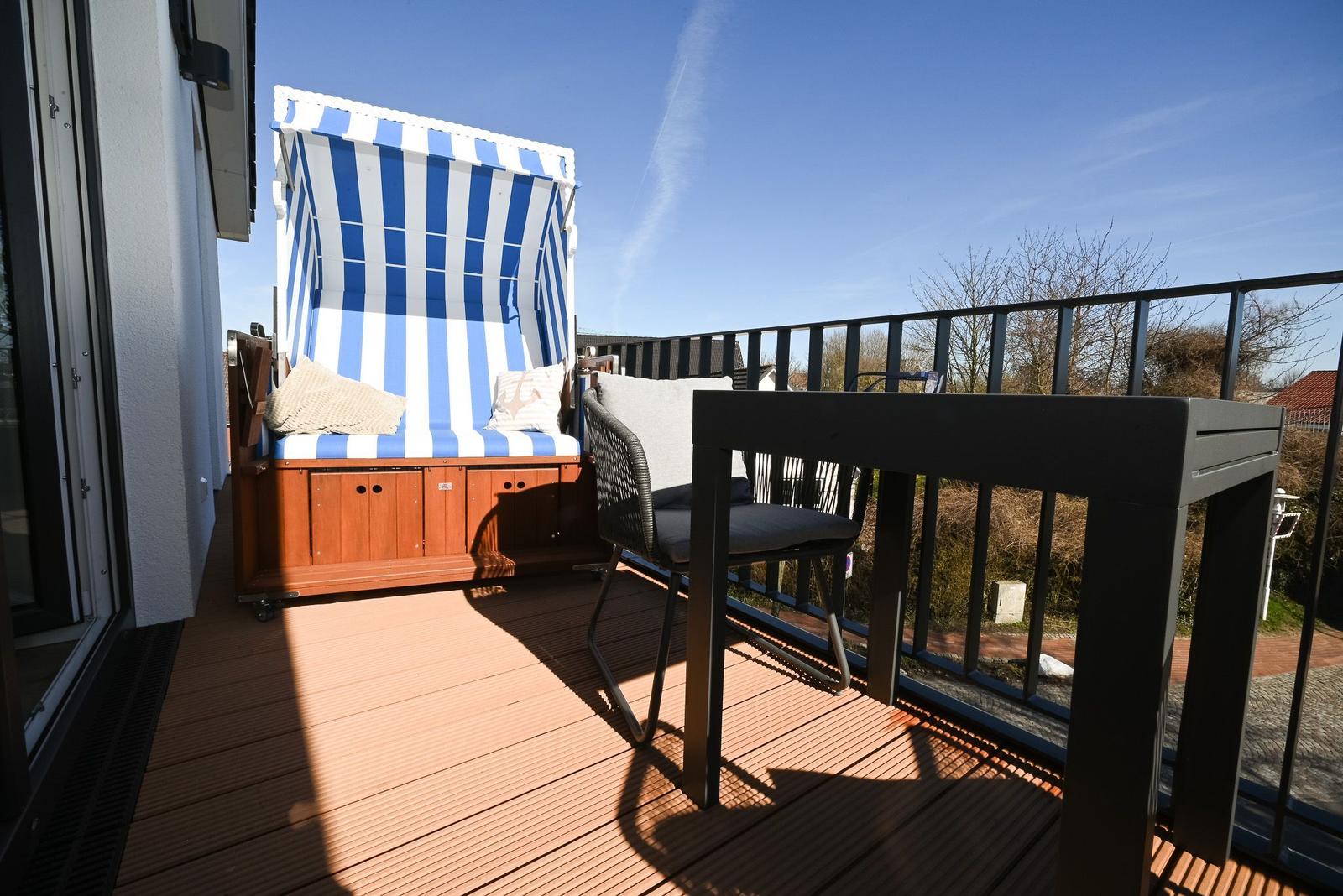 Terrasse mit Strandkorb, Tisch und Stuhl. Holzdecke und Metallgeländer.