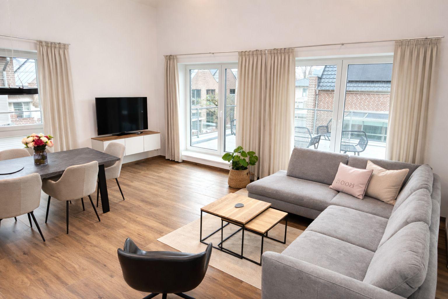 Wohn- und Essbereich mit Sofa, Tisch und TV. Durchgangstür zur Terrasse.