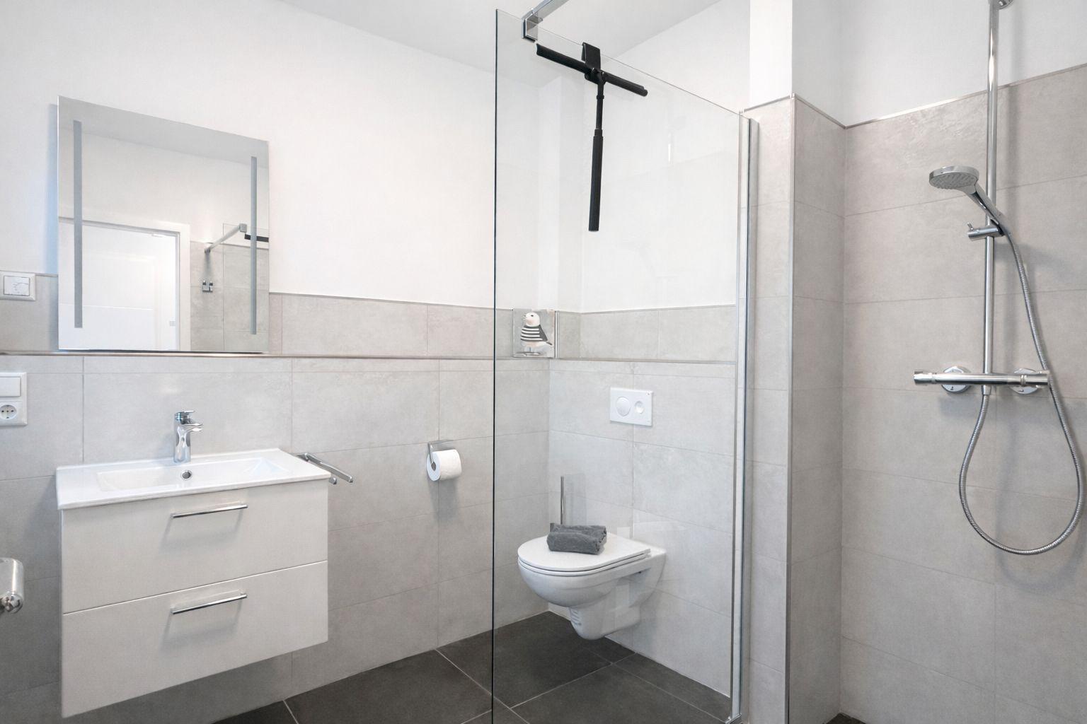 Badezimmer mit Dusche, Toilette und Waschbecken. Glaswand, Spiegel und Fliesen.