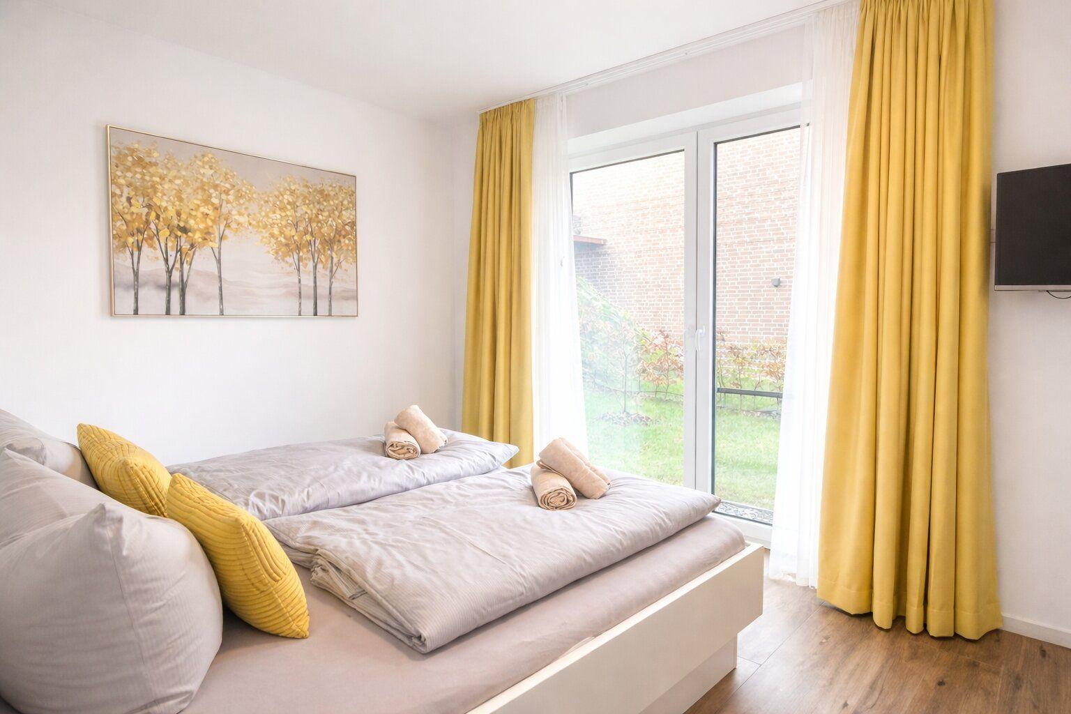 Schlafzimmer mit Bett, gelben Vorhängen und Fenster zur Außenansicht.