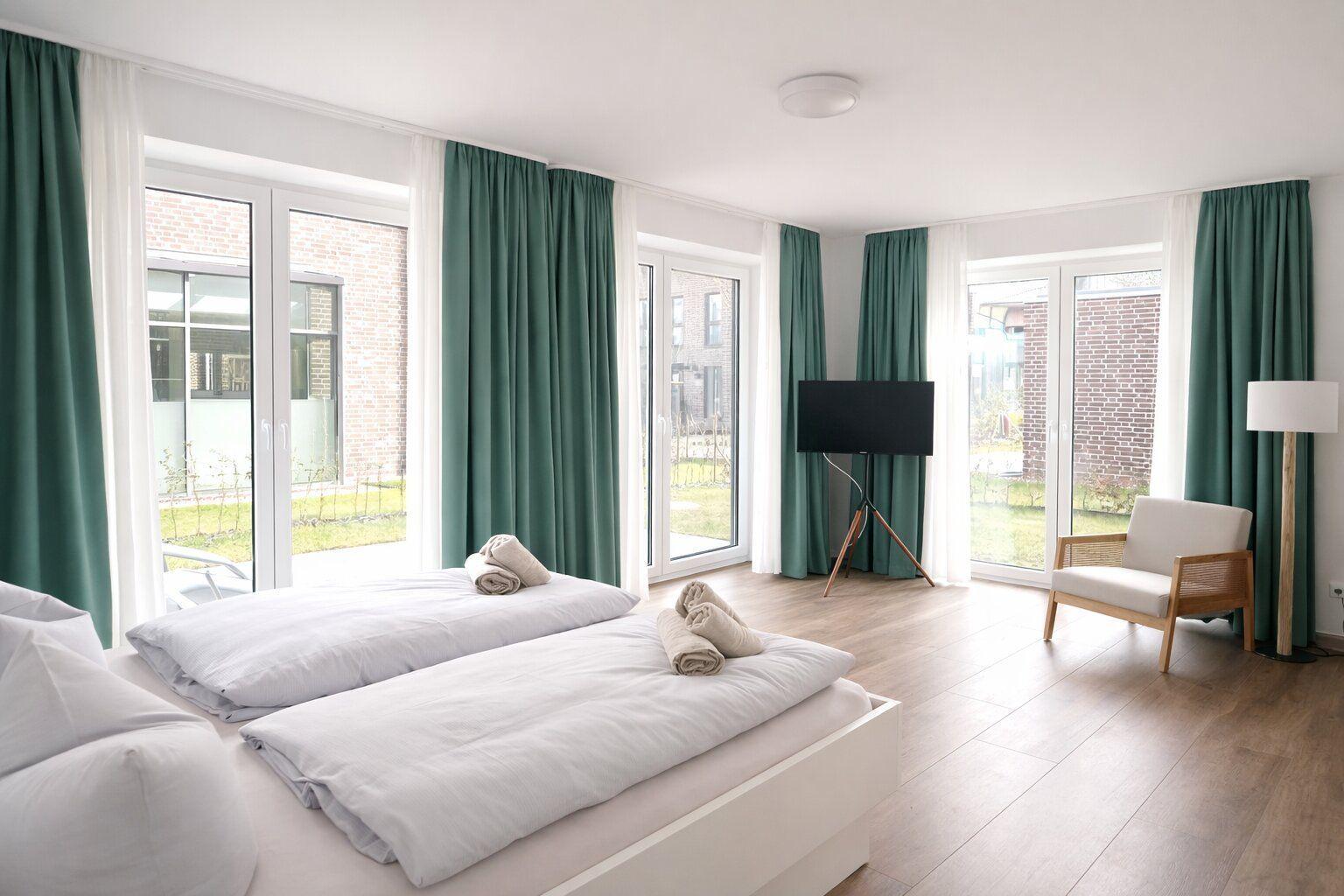 Zimmer mit zwei Betten, grünen Vorhängen und großem Fensterblick auf Außenbereich.