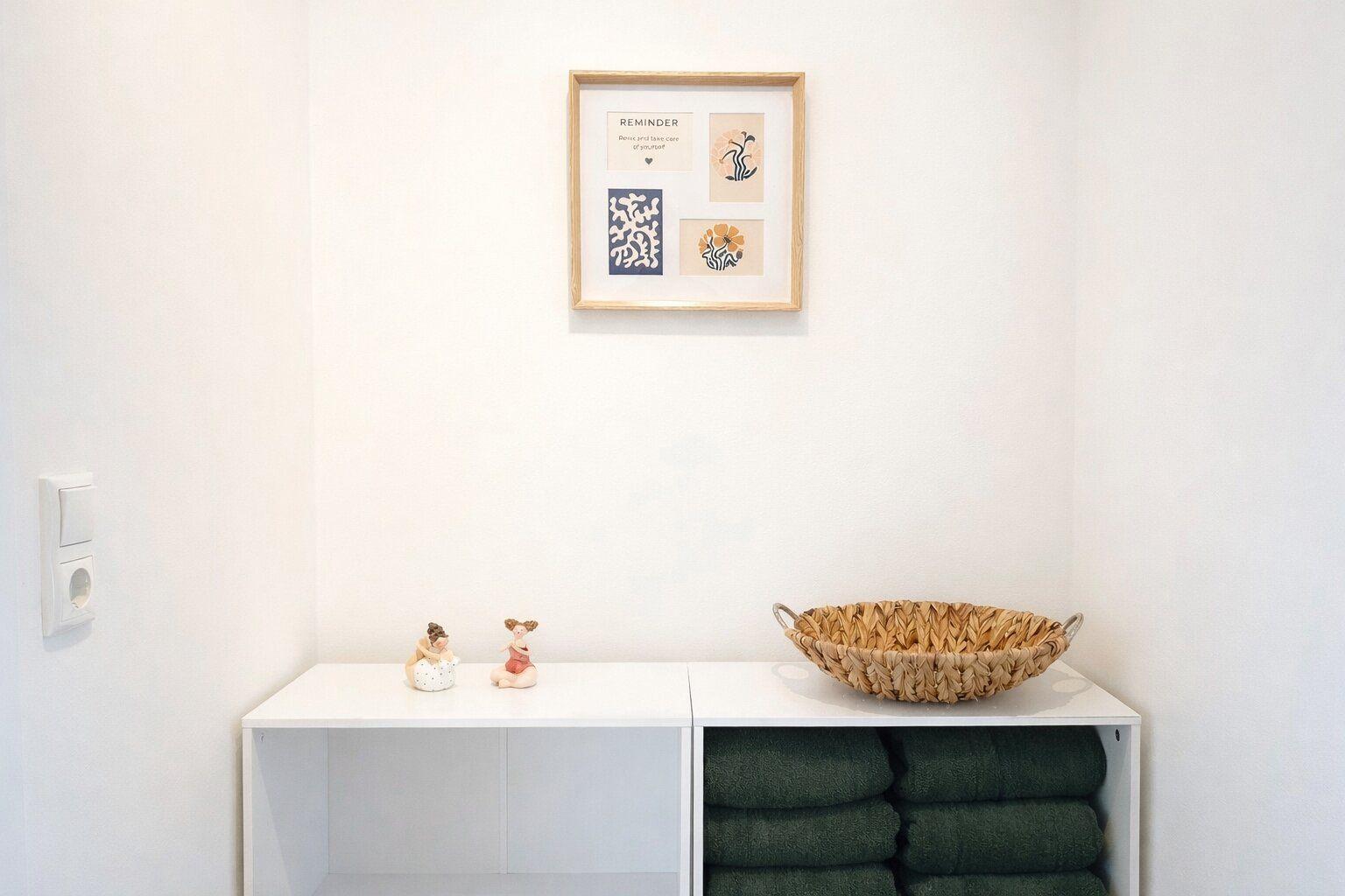 Wand mit Bild, weißer Schrank mit Handtuchstapel und Körbchen.