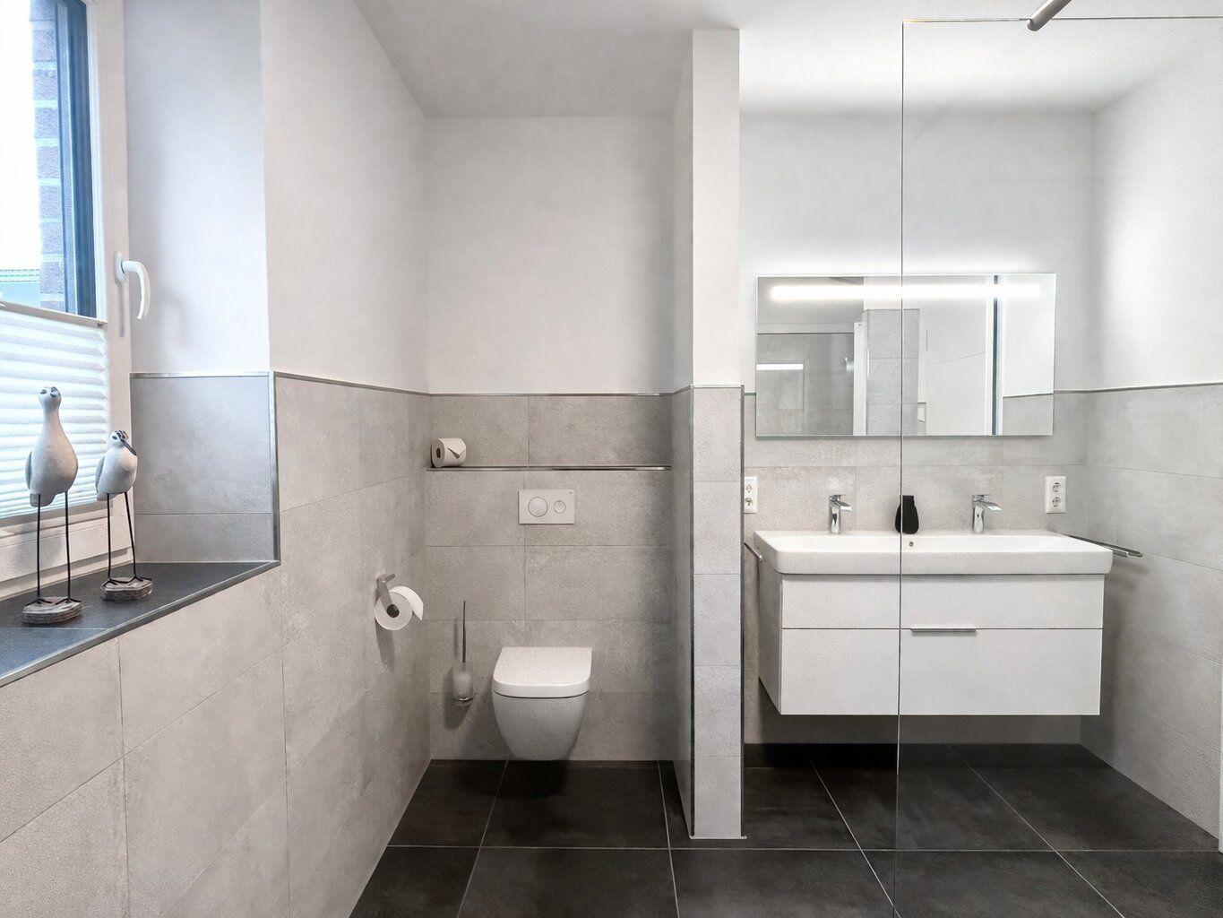 Badezimmer mit WC, Waschbecken und Spiegel. Fenster mit Vogeldekoration.