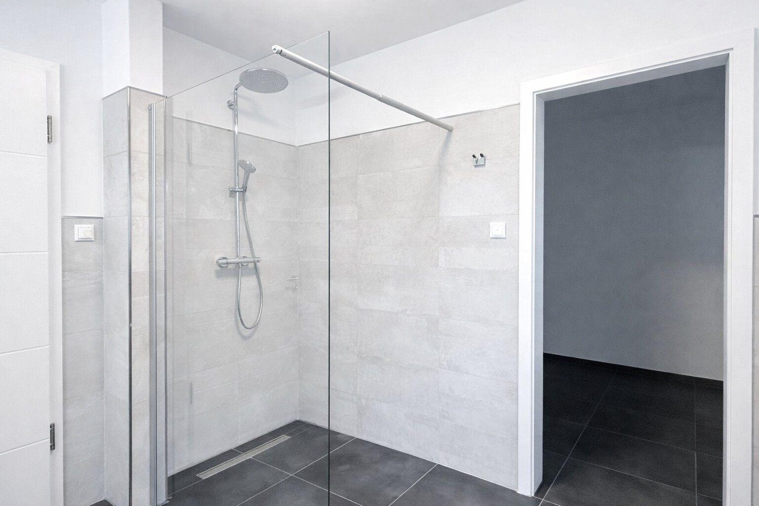 Dusche mit Glaswand, silbernen Armaturen und grauen Fliesen.
