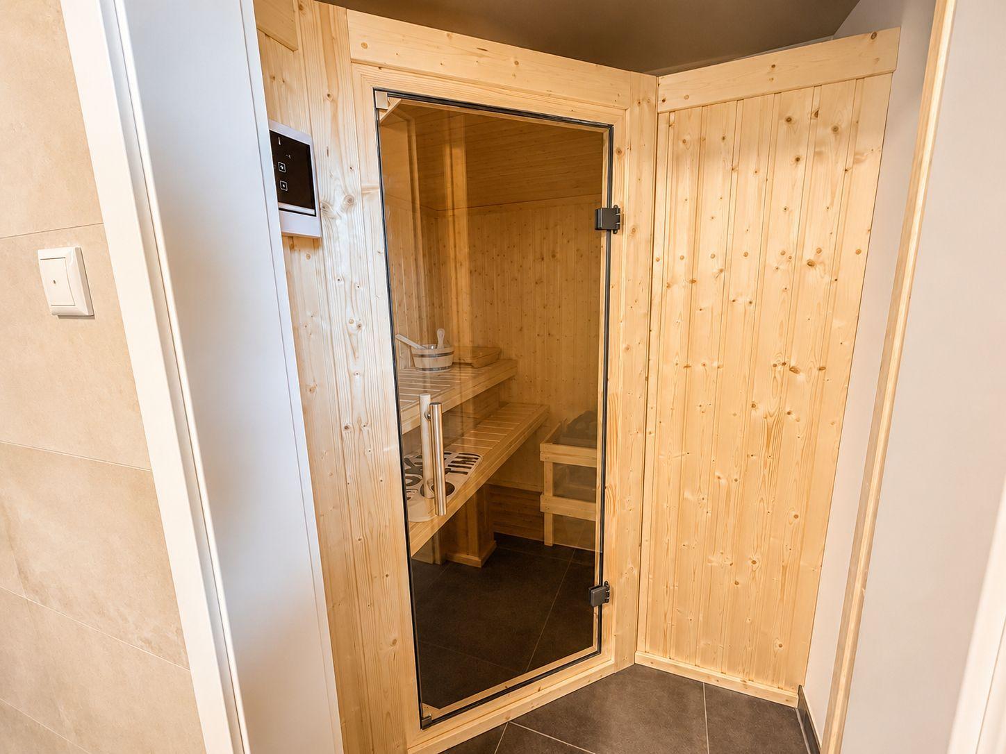 Sauna mit Holzwand, Sitzbänken und Glasfront. Bedienfeld an der Wand.