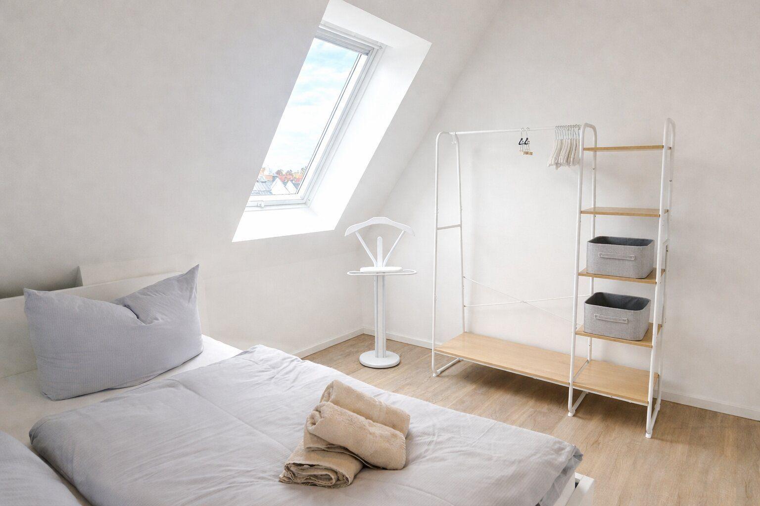 Schlafzimmer mit Dachschräge, Bett, Kleiderständer und Fenster.