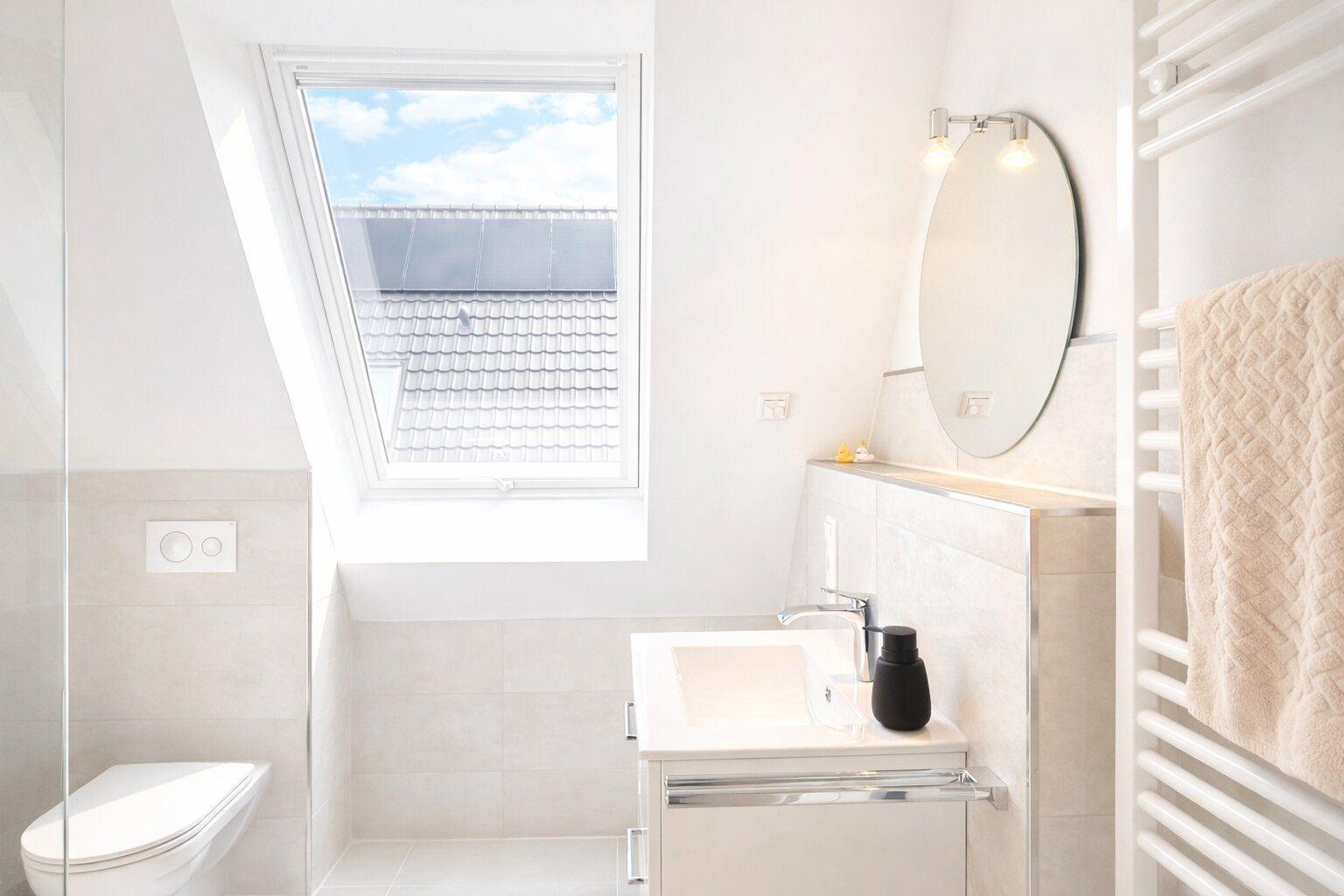 Badezimmer mit Dusche, Waschbecken und Dachfenster mit Blick auf Dach.