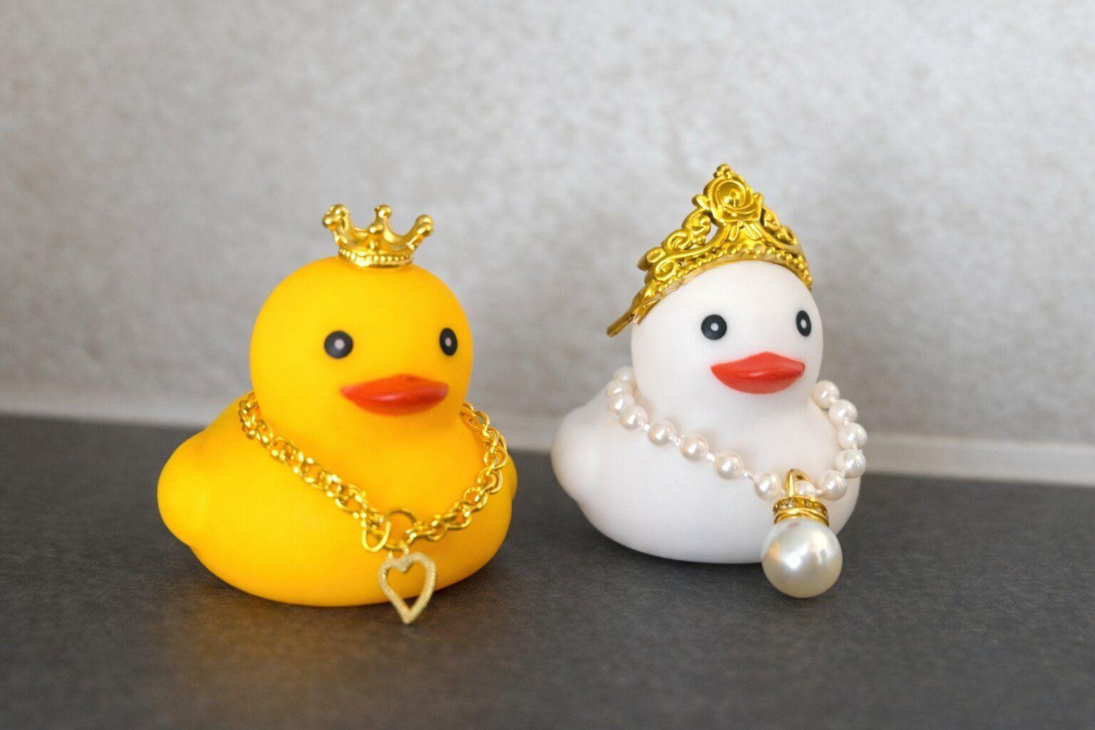 Zwei Schwimmkäfige, ein gelber mit goldenem Herzanhänger und ein weißer mit Perlenkette und Krone.
