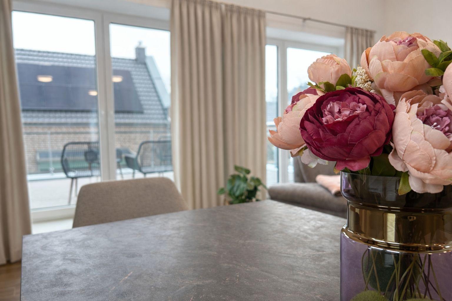 Tisch mit Blumenarrangement und Blick auf Balkon mit Sitzgelegenheiten.