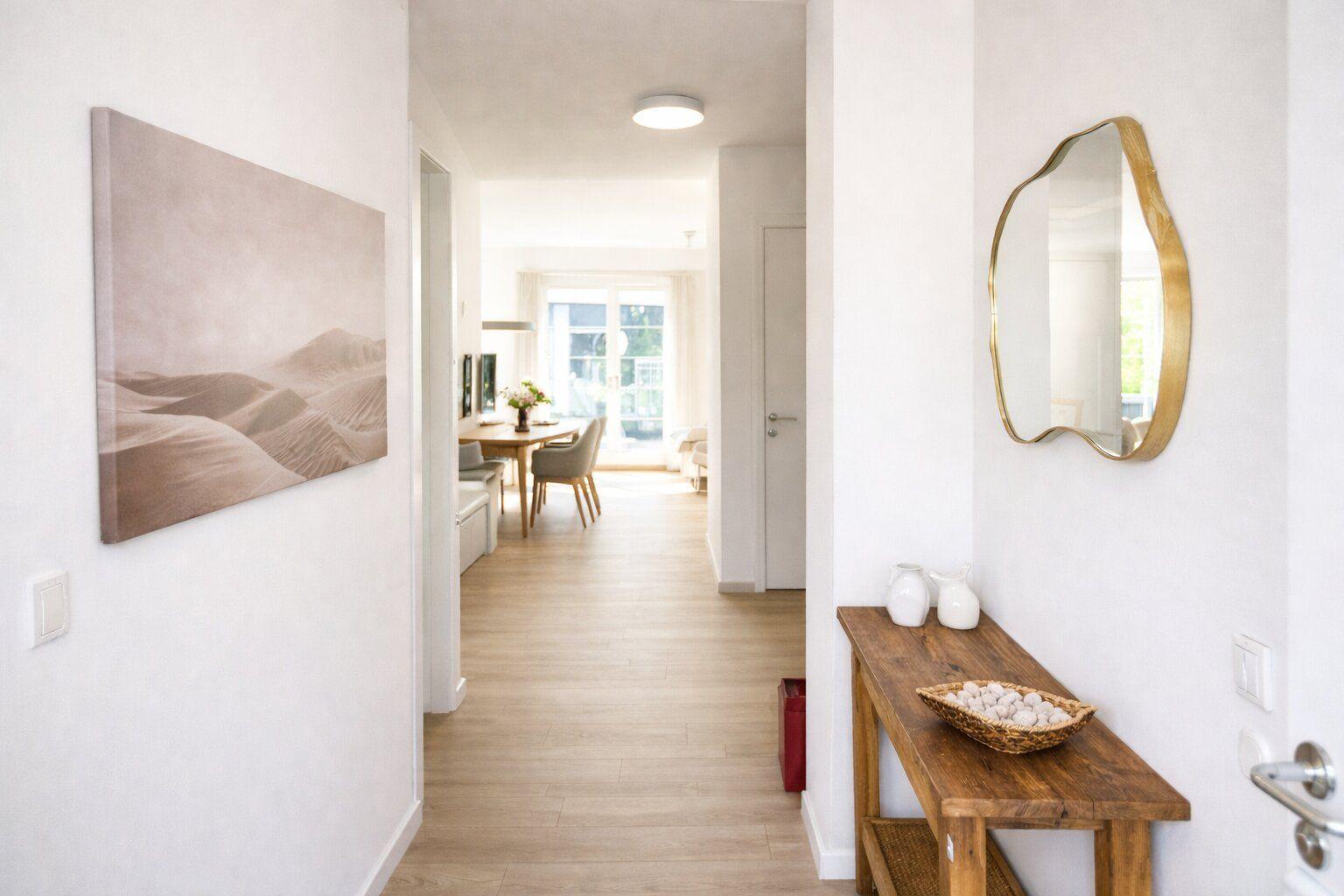 Flur mit Wandbild, Spiegel und Holzbank. Blick in Wohn- und Essbereich.