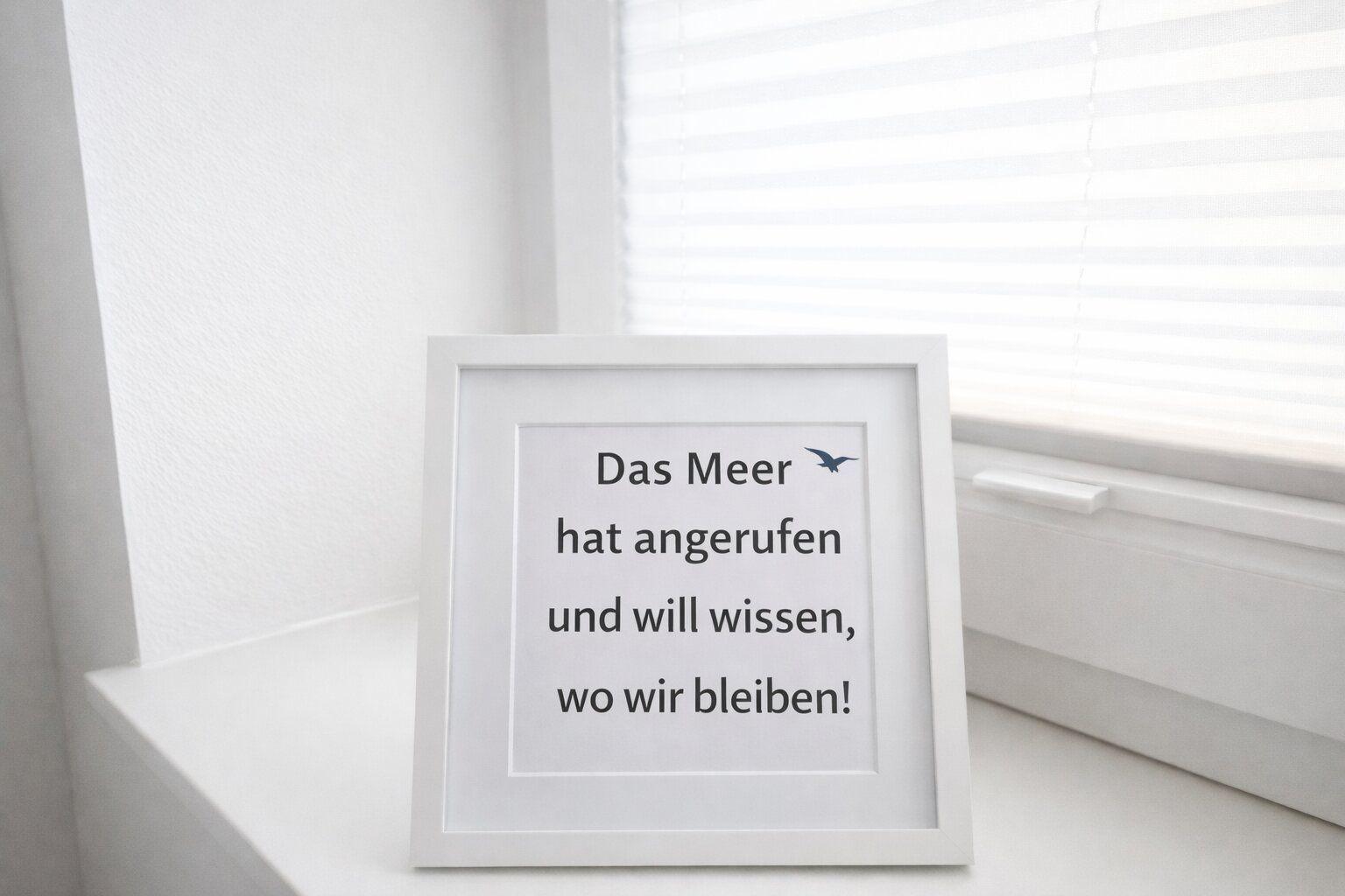 Ein gerahmtes Schild mit Text steht auf einem Fensterbrett. Im Hintergrund sind Jalousien zu sehen.