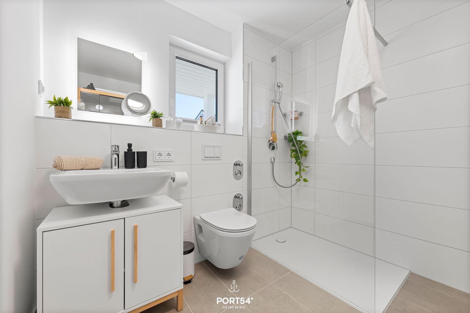 Badezimmer mit Dusche, Waschbecken und Toilette. Weiße Fliesen und Holzgriffe.