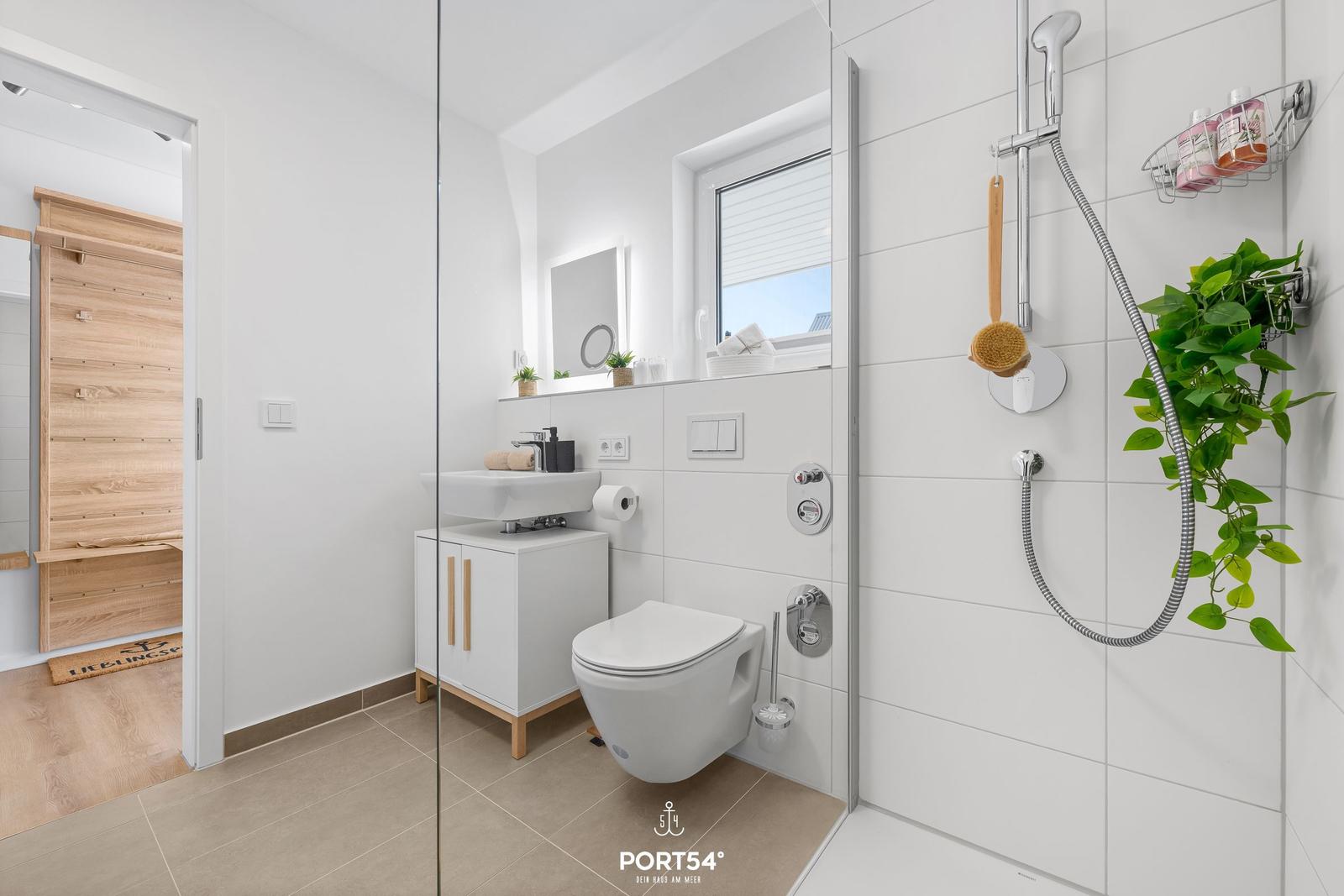 Badezimmer mit Dusche, WC und Waschbecken. Holzoptik und Pflanze sichtbar.