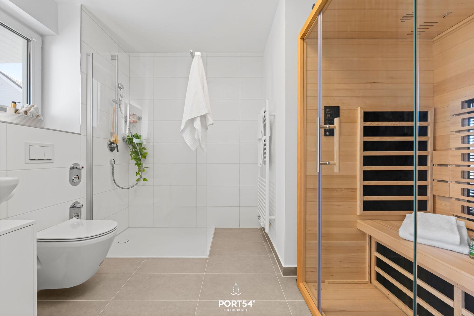 Bad mit Dusche und Sauna. Weiße Fliesen, Holzsauna mit Sitzbank.