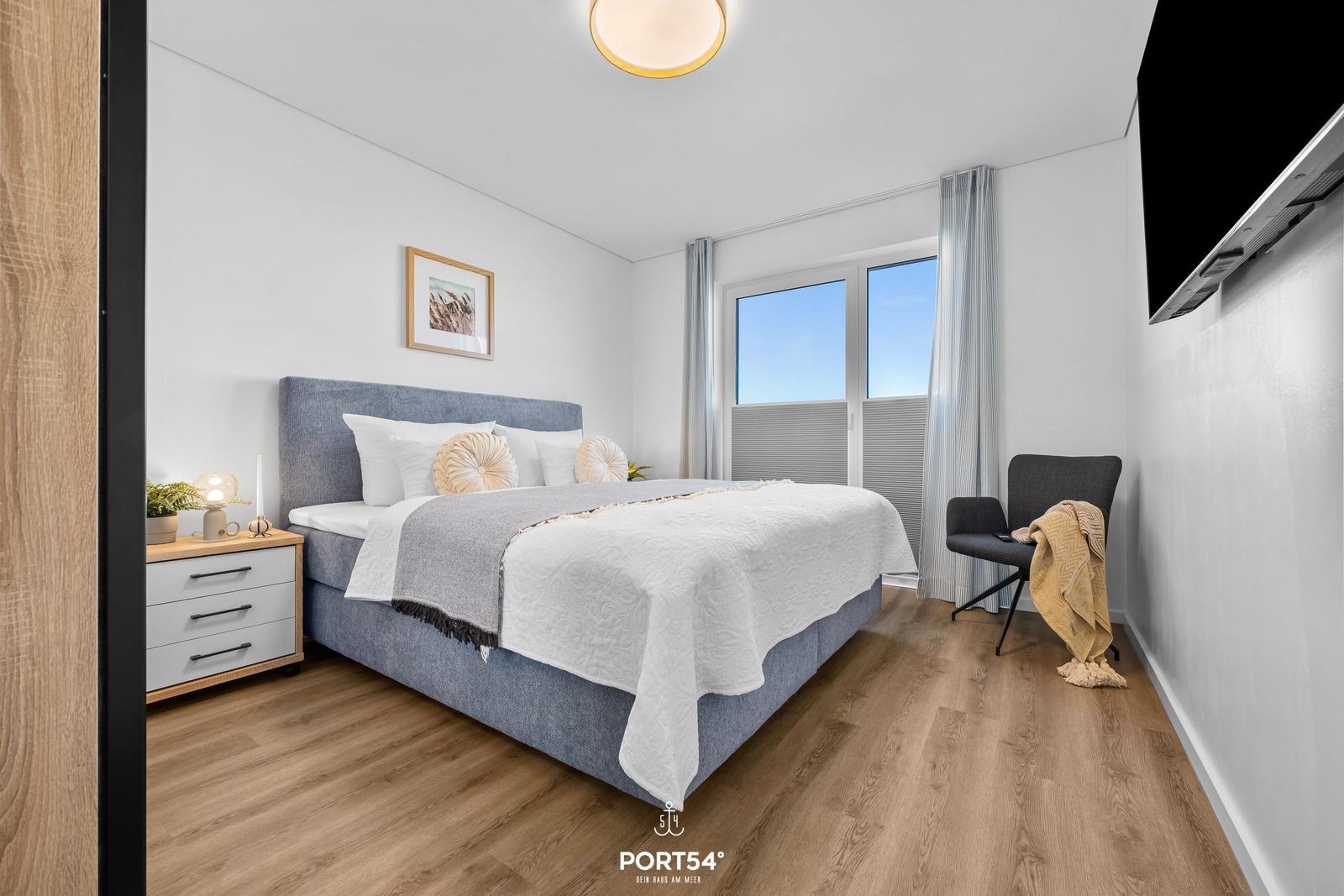 Schlafzimmer mit Bett, Nachttisch und Fenster. Holzboden und Wandbild.