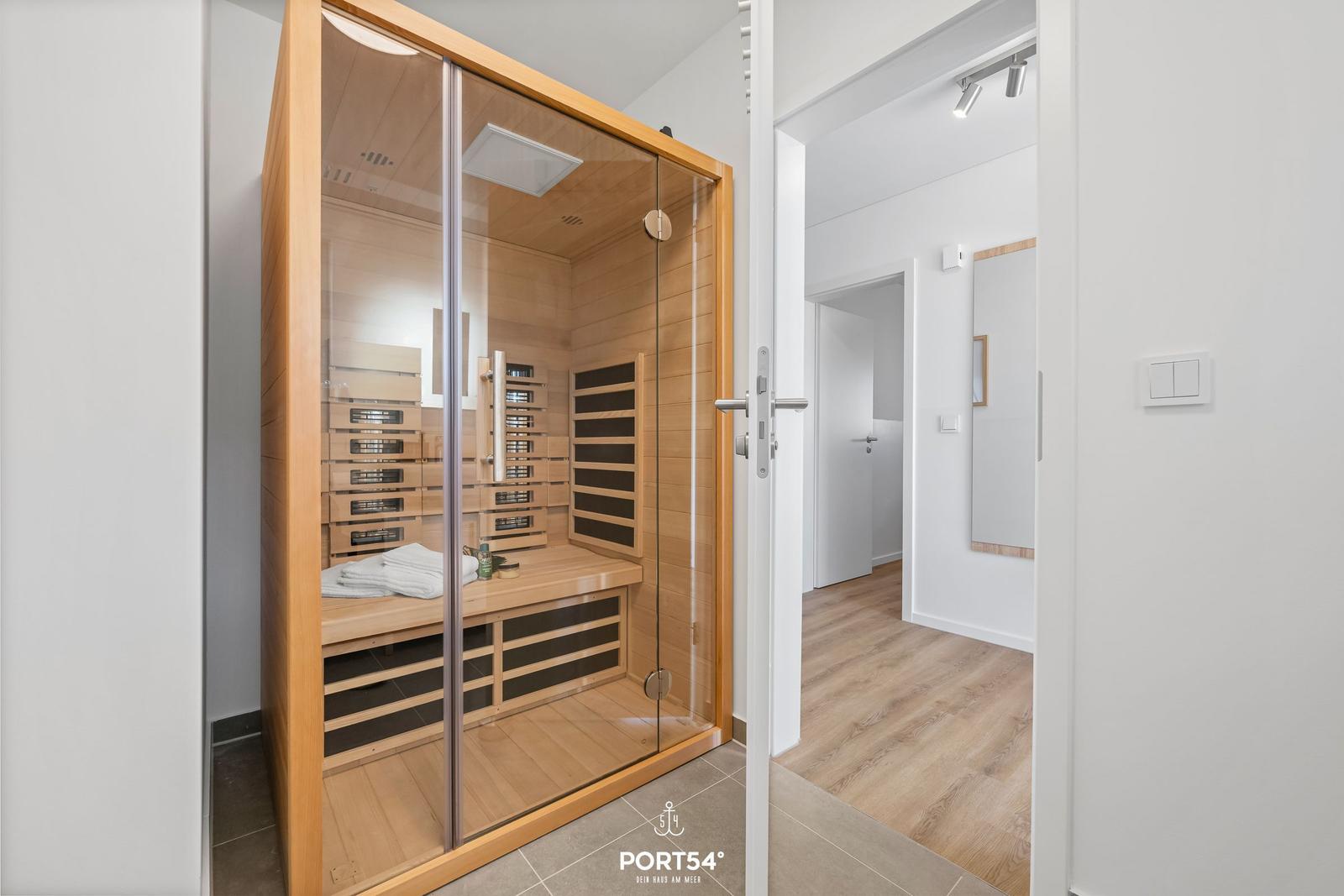 Innere Sauna mit Holzverkleidung und Glasfront. Weiße Wände und Holzboden sichtbar.