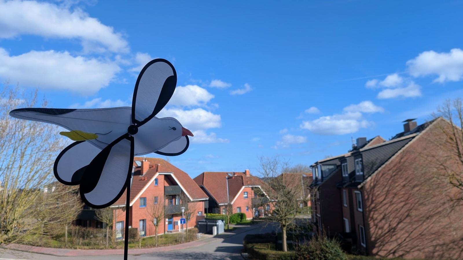 Windspiel in Form einer Möwe vor Wohnhäusern unter blauem Himmel.