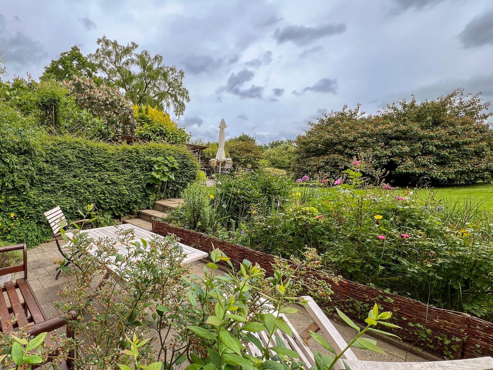 Garden with terrace, garden furniture, and flower beds under cloudy sky.