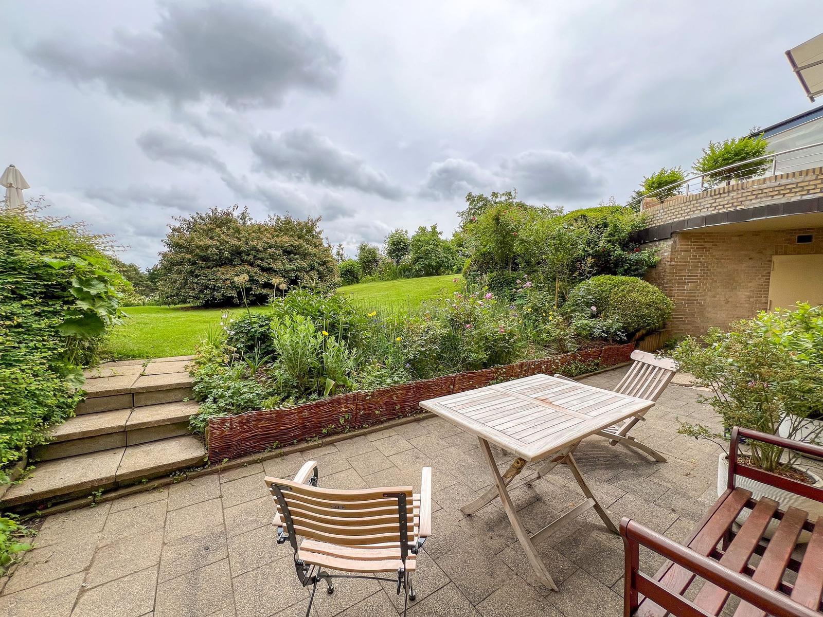 Terrace with table and chairs, view of green garden and lawn.