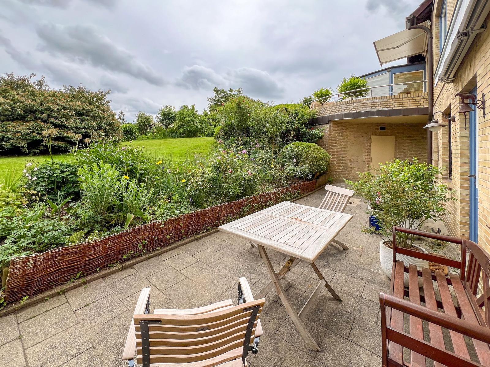 Terrace with table and chairs, surrounded by garden and house.