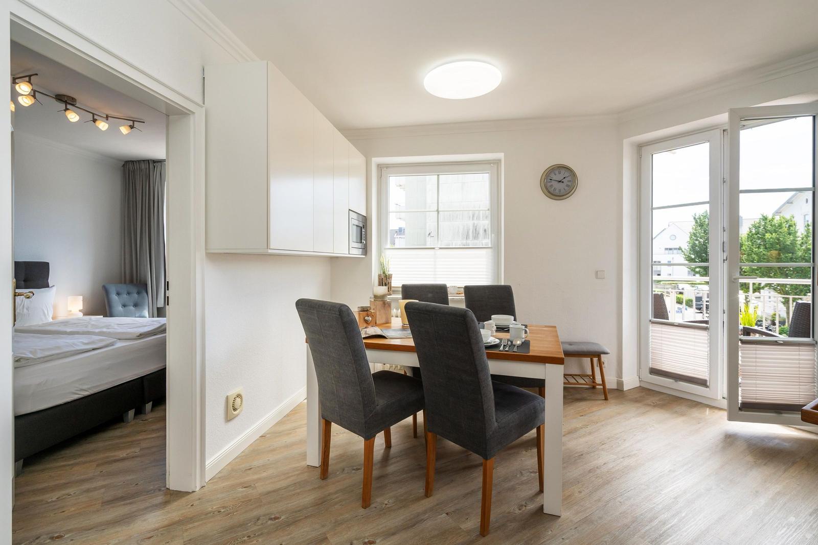 Essbereich mit Tisch und Stühlen, Küchenzeile und Blick auf Balkon. Schlafzimmer im Hintergrund.