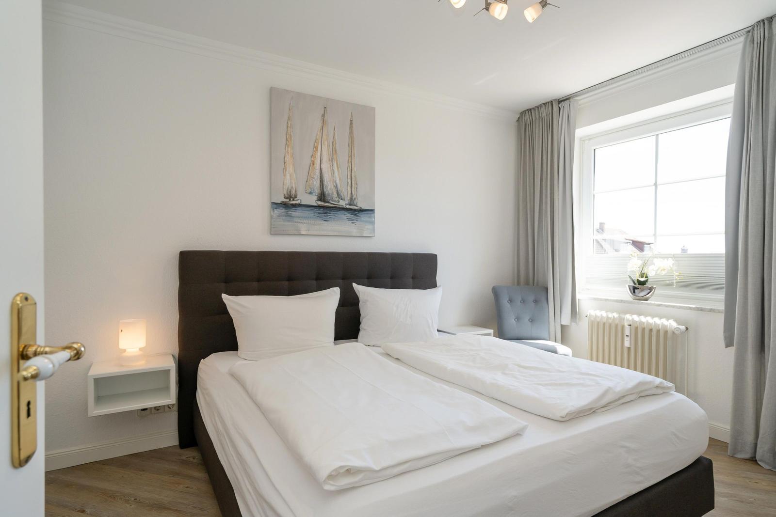 Schlafzimmer mit Doppelbett, Wandbild und Fenster mit Vorhängen.
