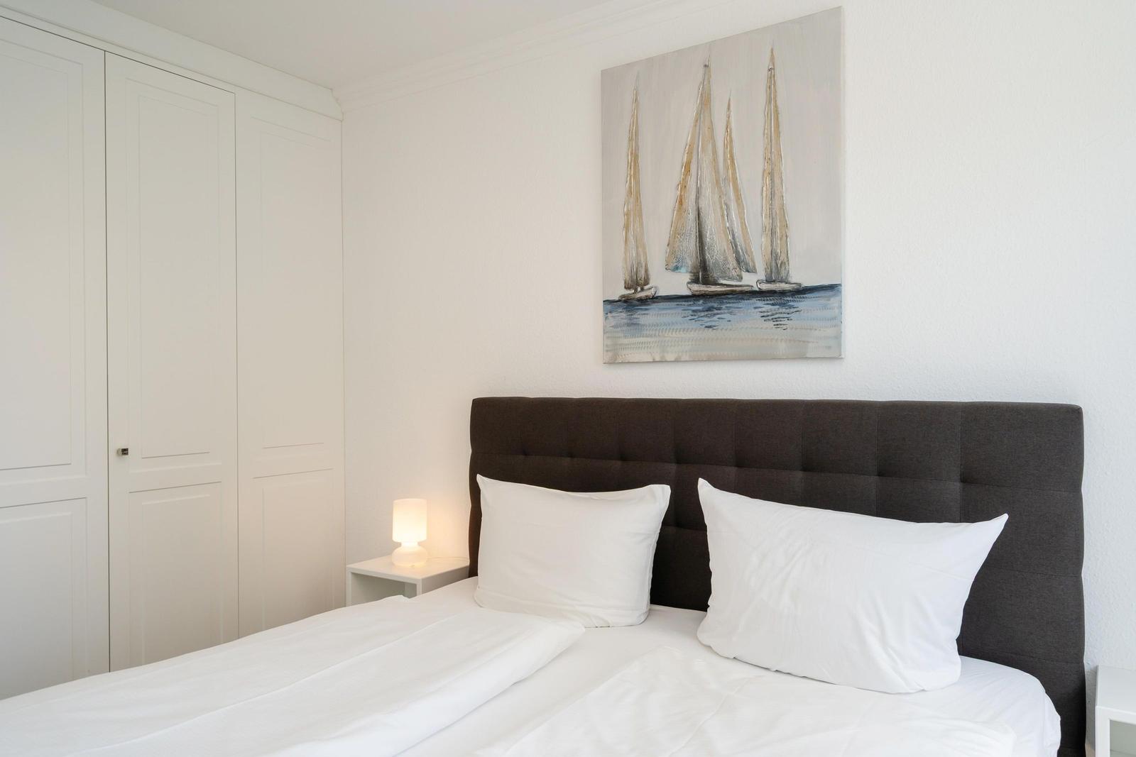 Schlafzimmer mit Bett, Nachttisch und Wandbild mit Segelbooten.