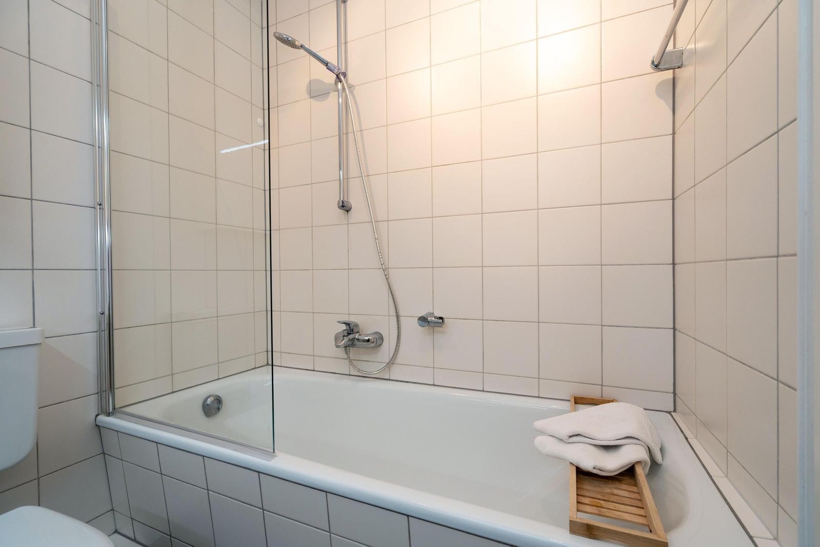 Bad mit Badewanne, Duschkopf und Handtuch auf Holztablett.