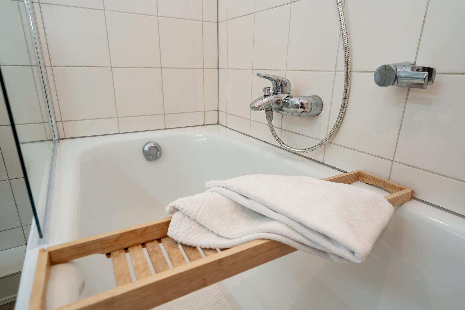 Badewanne mit Duschbrause und Holzablage für Handtücher.
