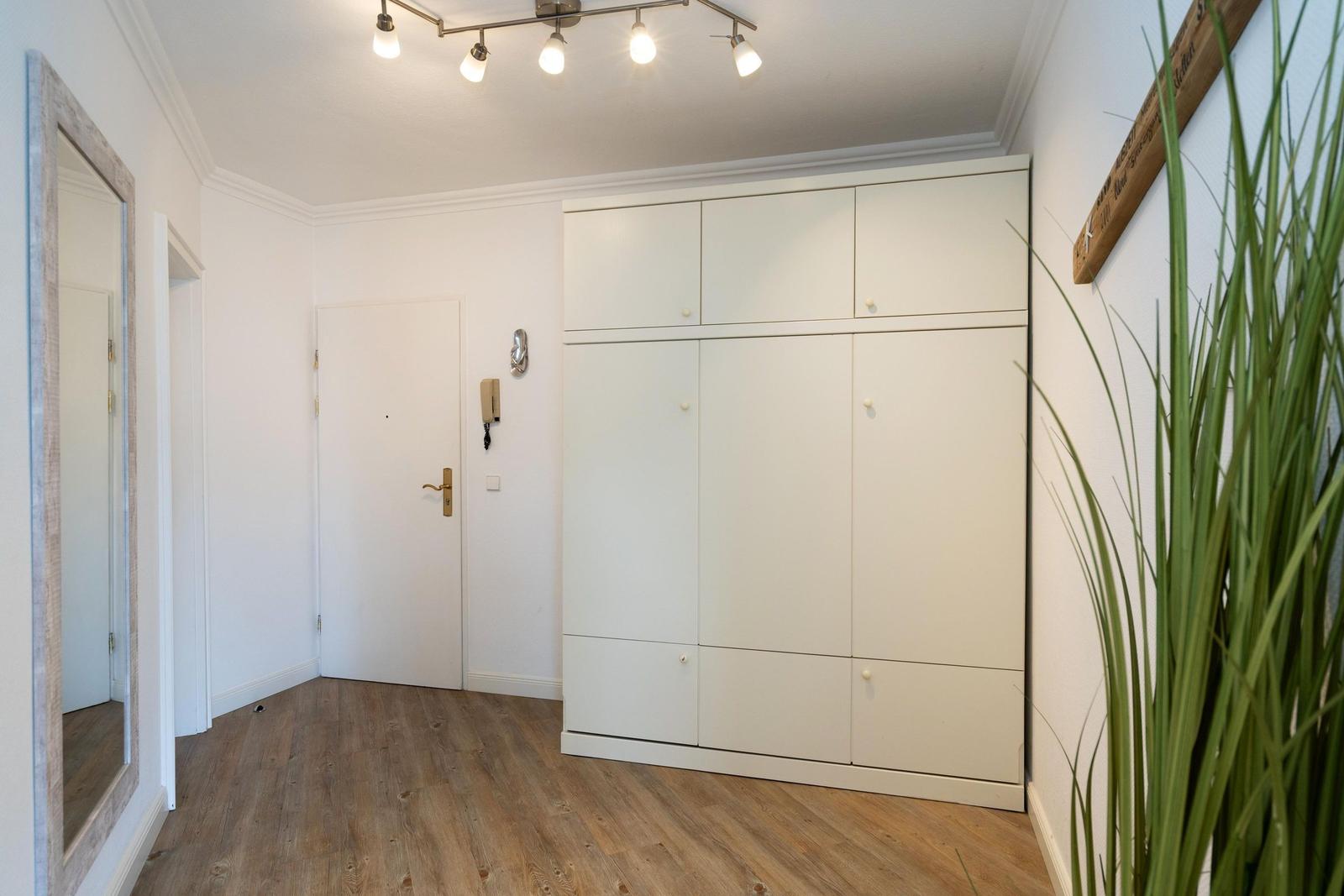 Eingangsbereich mit weißen Schränken, Holzboden und Pflanze an der Wand.