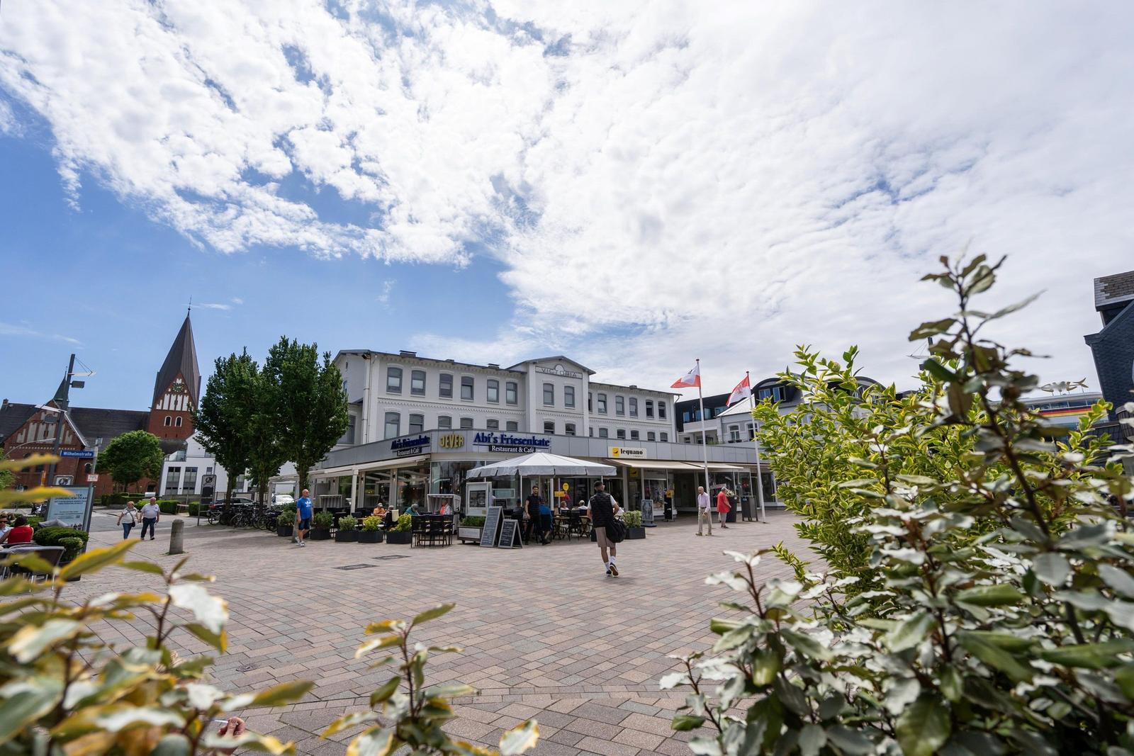 Marktplatz mit Café, Restaurants und historischem Turm unter blauem Himmel.