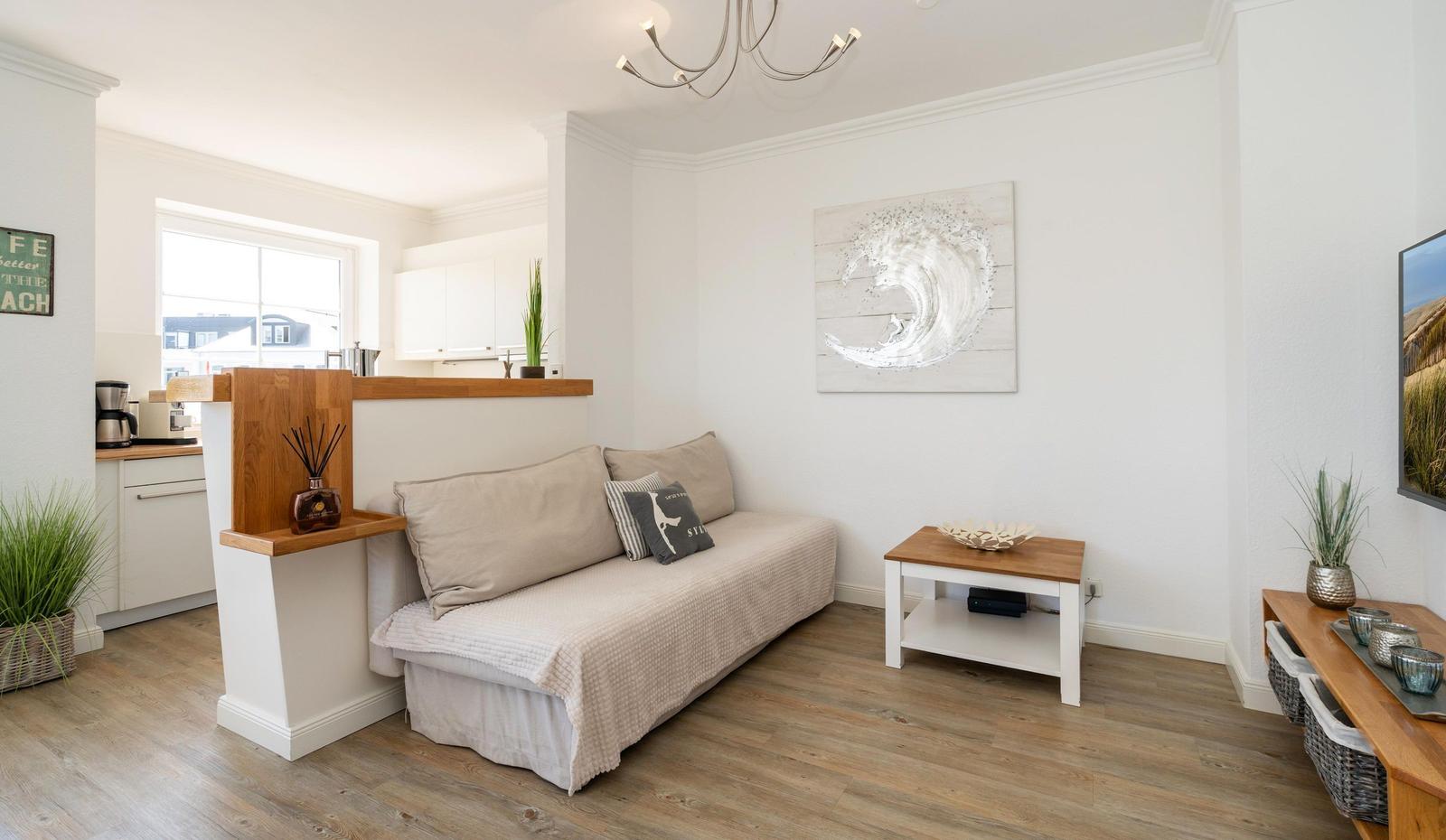 Wohnbereich mit Sofa, Tisch und Wandbild. Küche im Hintergrund.