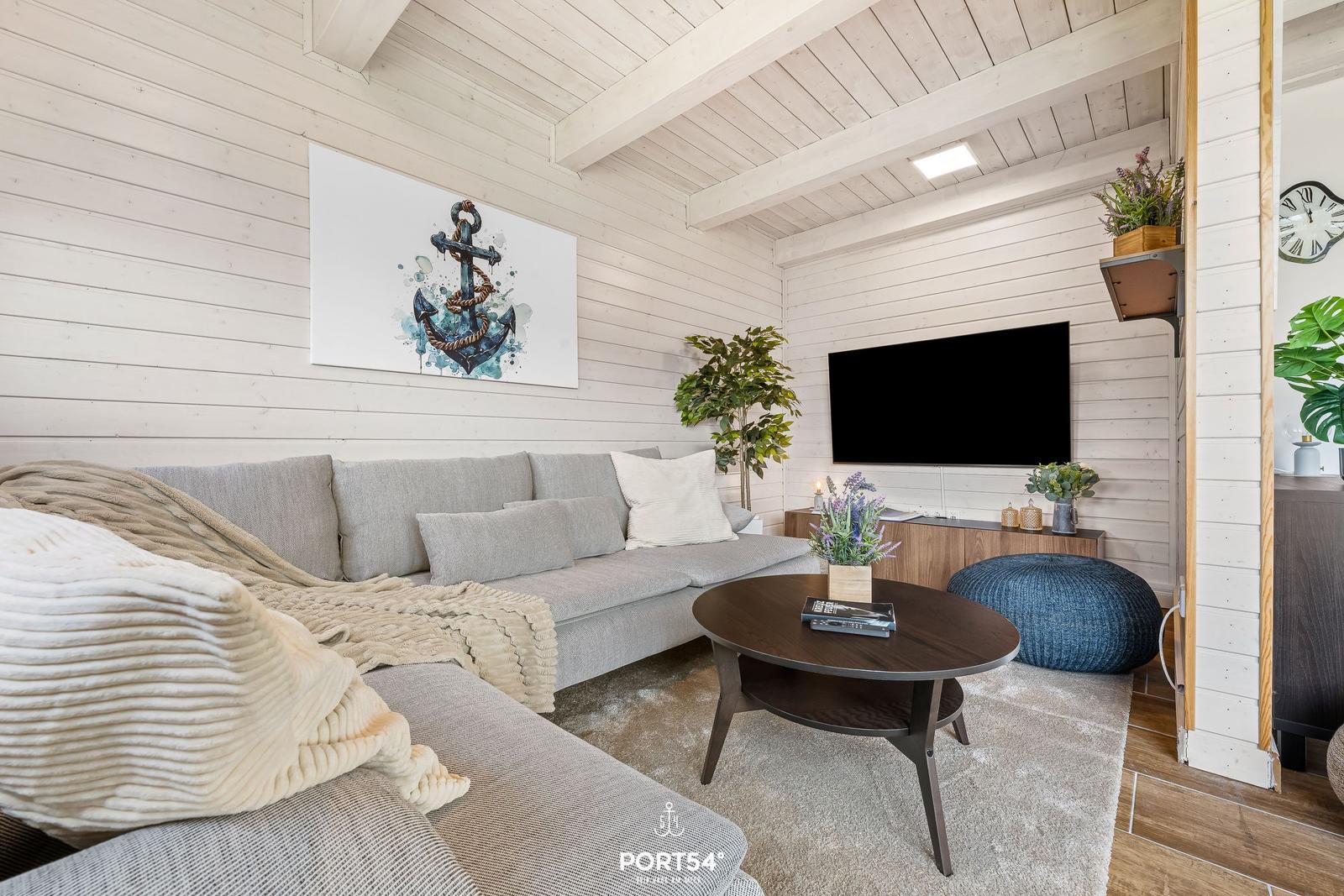 Wohnzimmer mit Sofa, Couchtisch und Fernseher an weiß verputzten Wänden.