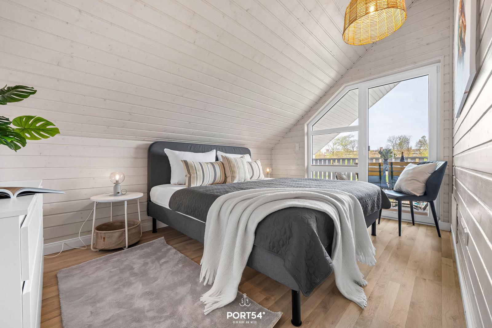 Schlafzimmer mit Dachschräge, Bett, Fenster und Stuhl.